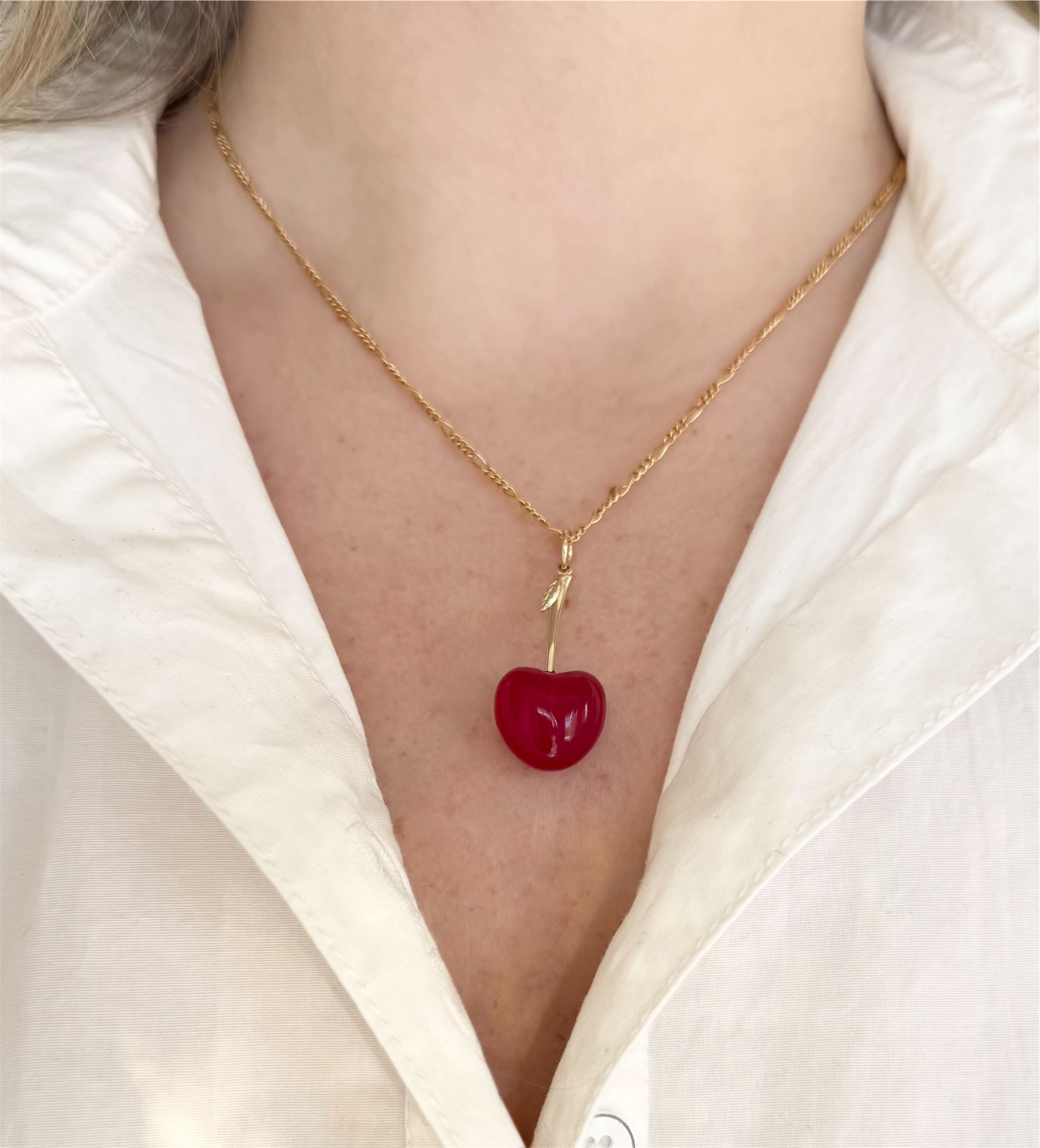 Gold necklace with a red cherry pendant worn by a person in a white shirt.