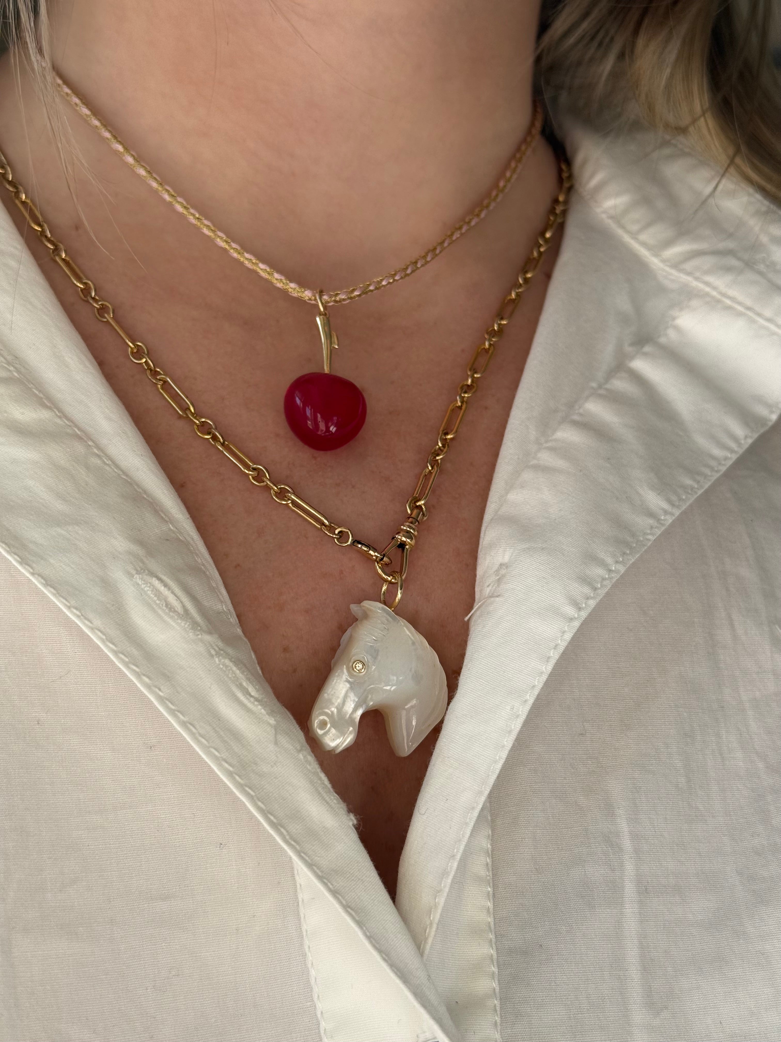 Necklace with horse pendant and red berry charm worn by a person in a white shirt.