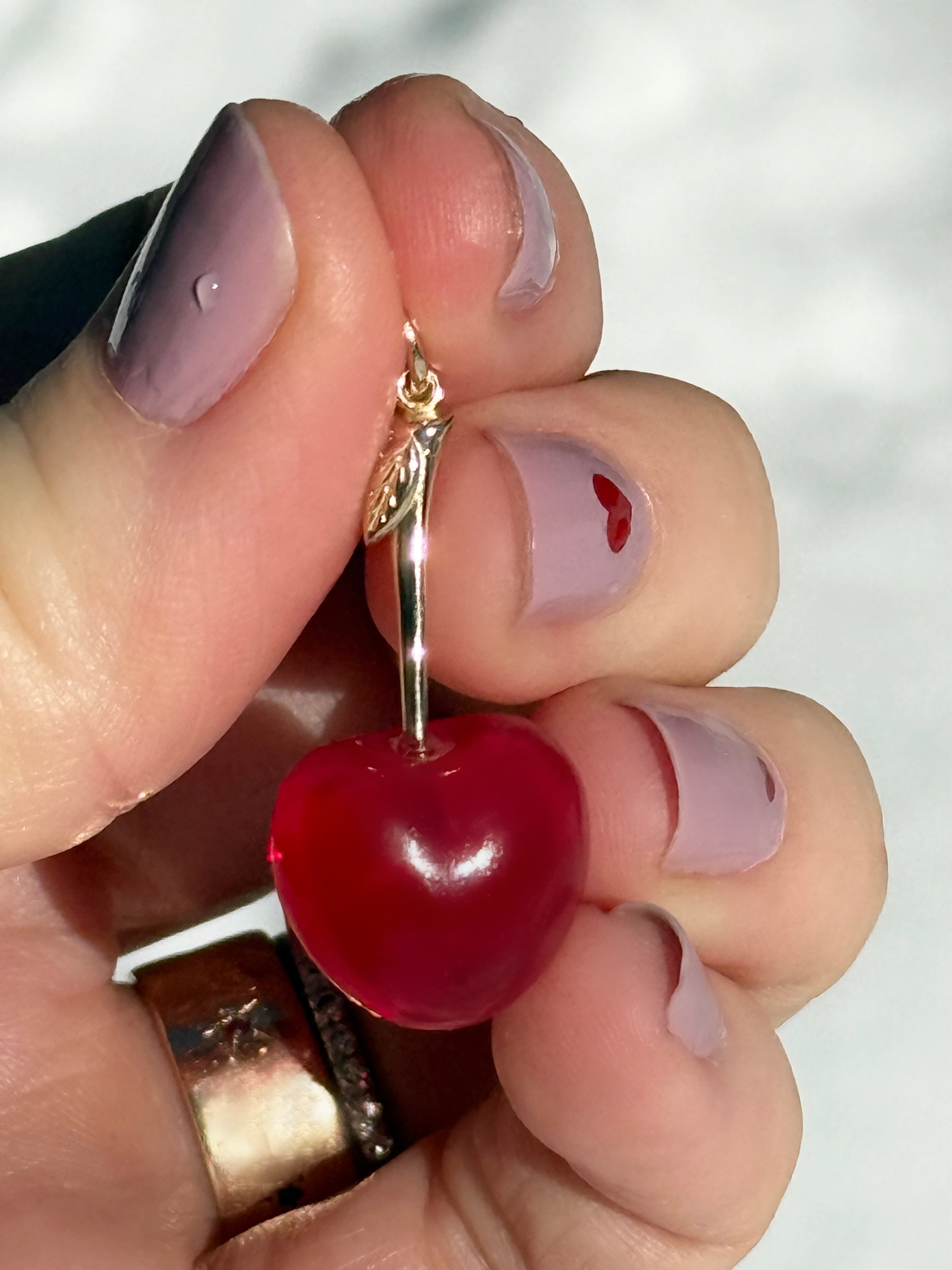 Hand holding a cherry-shaped charm with gold detailing against a white background.