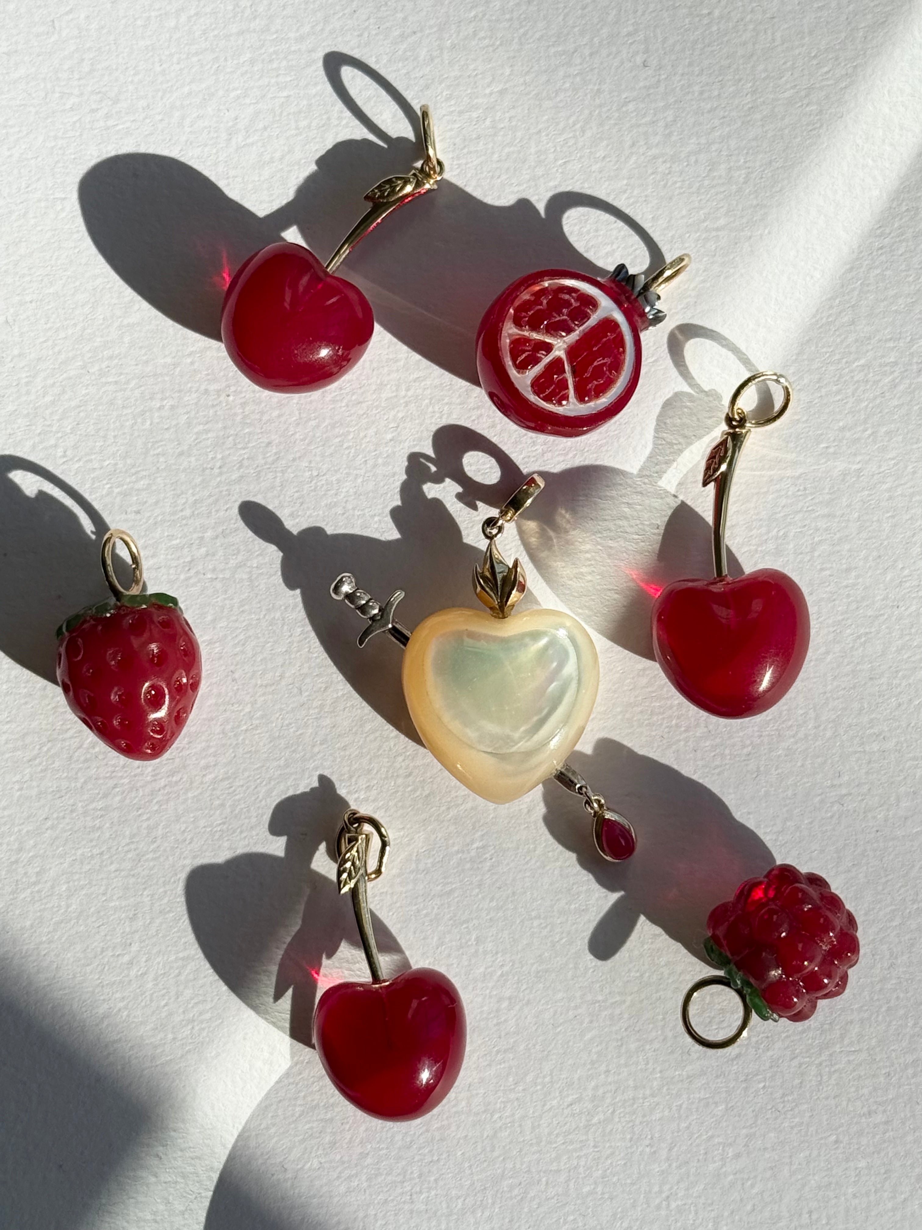 Sacred heart charm surrounded by pomegranate, raspberry, strawberry, and cherry drop charms on a white background, designed by Maura Green