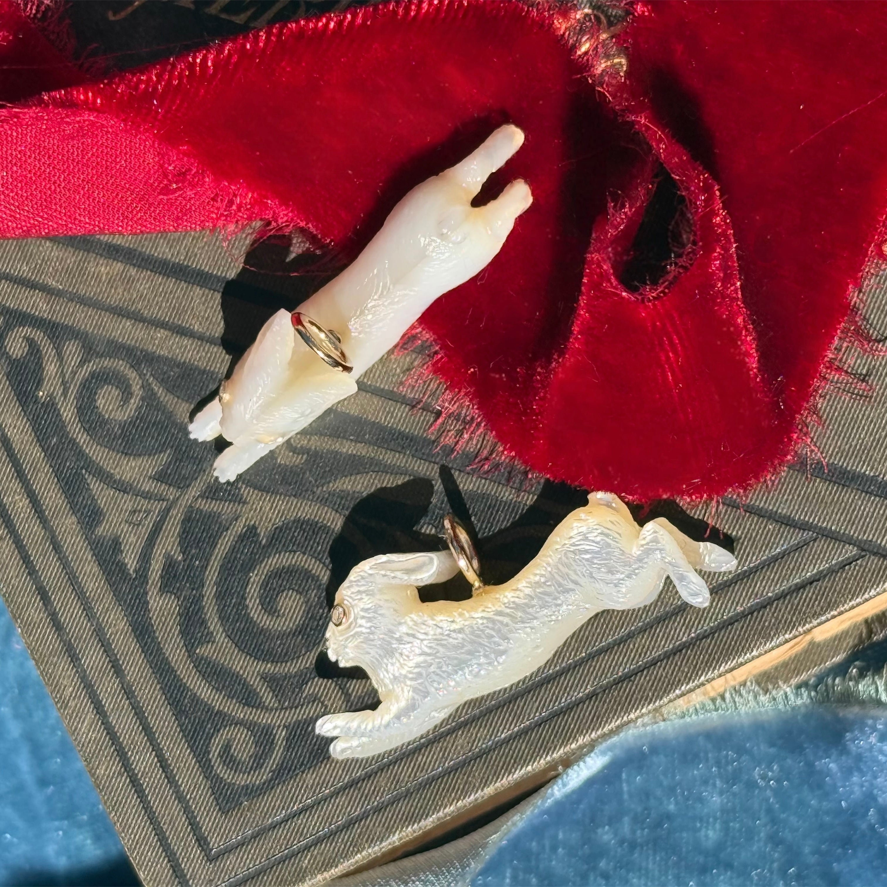 Two white leaping rabbit charms on a red fabric background. Designed by Maura Green