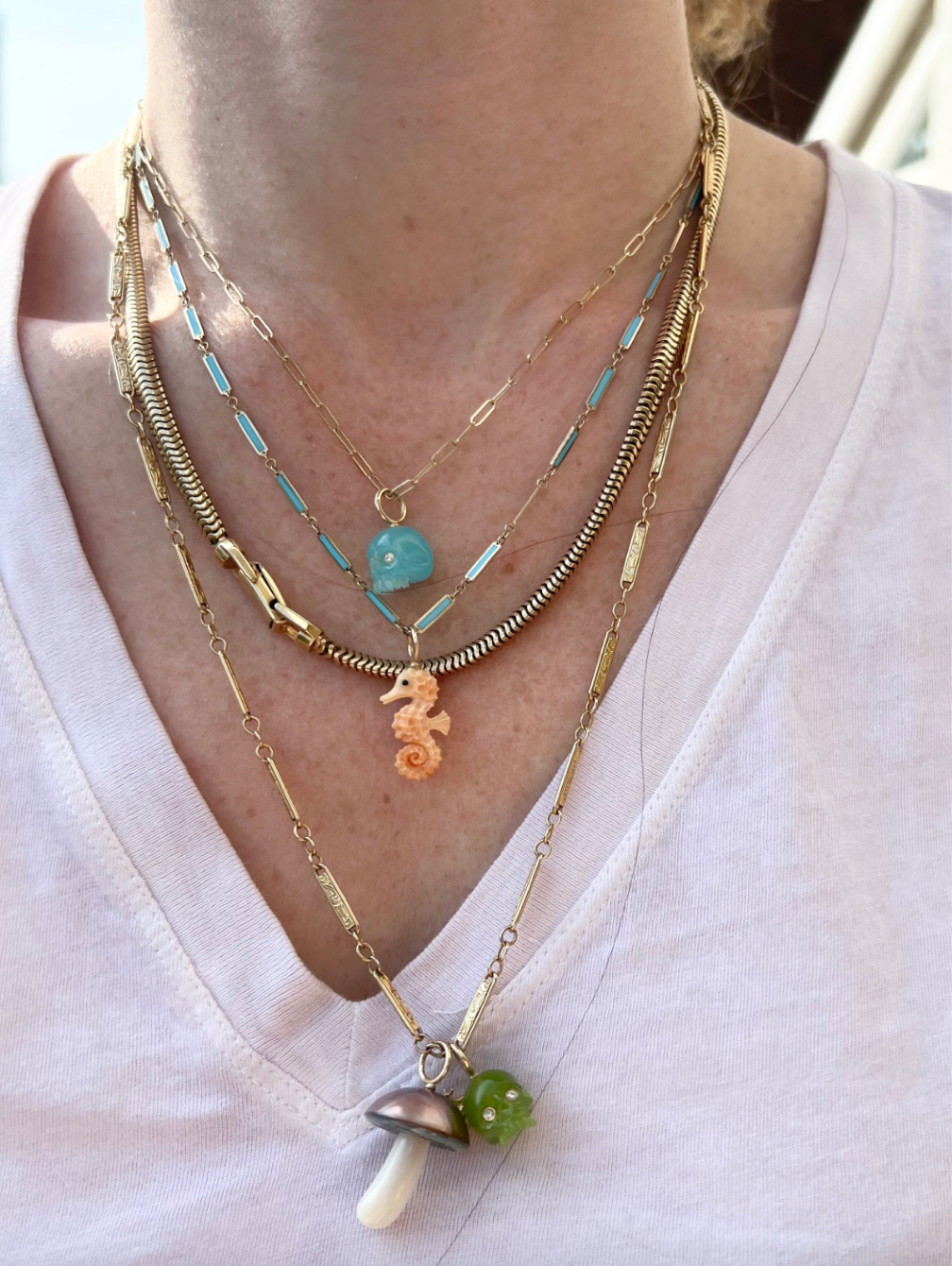 A gold-colored seahorse charm made from apricot conch shell on a blue and gold chain worn by model designed by Maura Green.