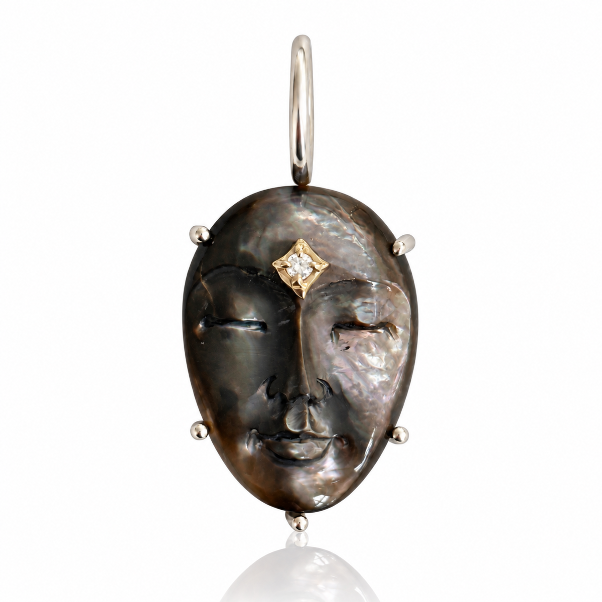 A detailed pendant featuring a stylized woman's face crafted from dark mother-of-pearl with a small gold diamond accent on the forehead, set in silver-tone metal with a hanging loop at the top. Designed by Maura Green