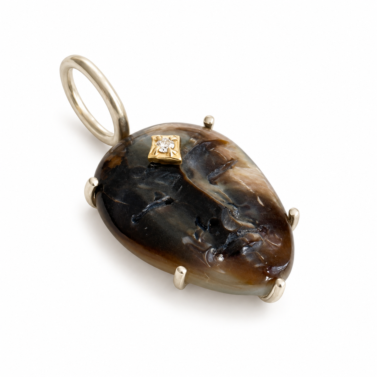 A charm shaped like a woman's face carved out of black mother of pearl with a 14K gold star shaped diamond accent on it's forehead, shown on a white background. The setting and bail are sterling silver. Designed by Maura Green