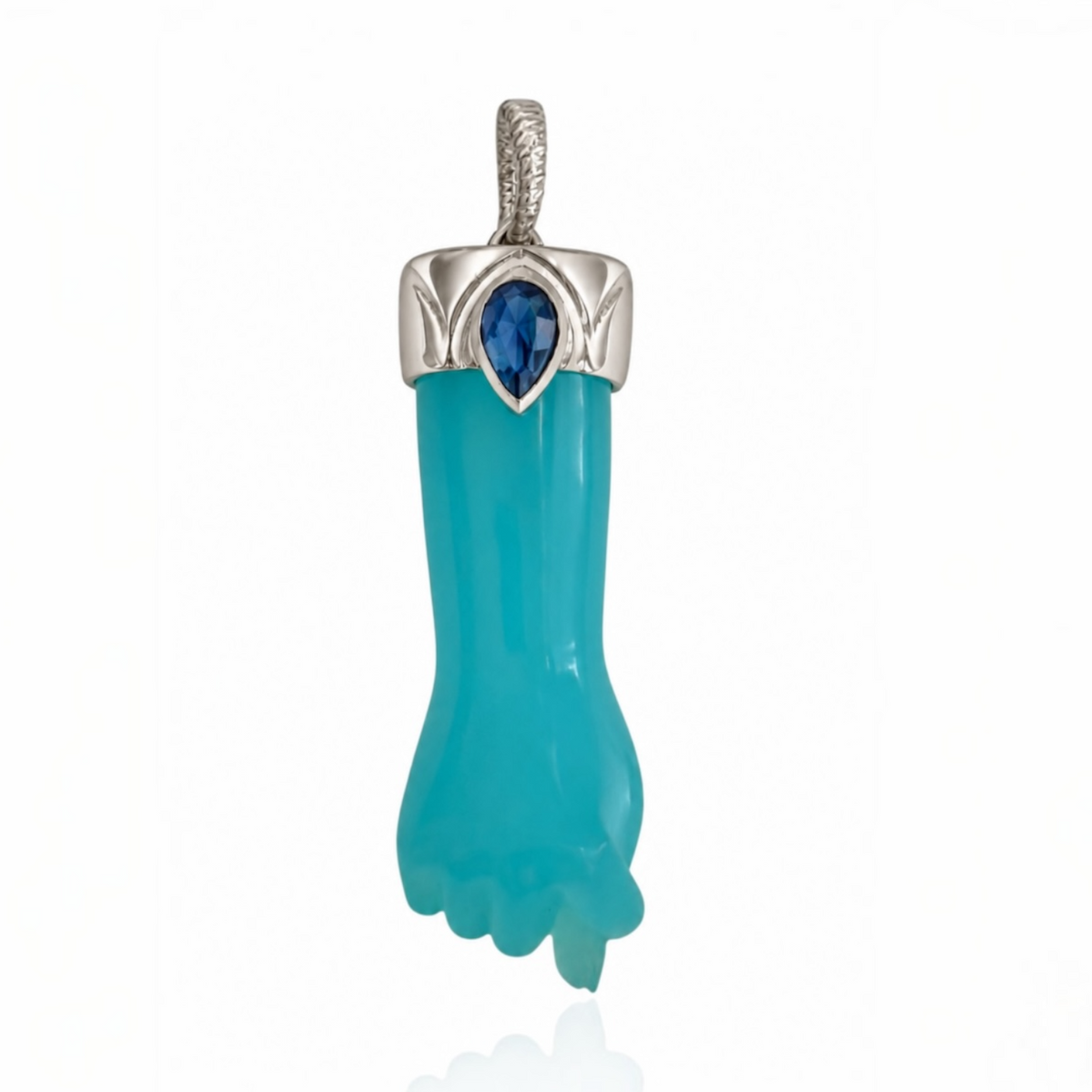 Hand-carved blue chalcedony mano figa charm with a sterling silver engraved cap, blue sapphire teardrop accent, and silver bail against a white reflective background. Designed by Maura Green.