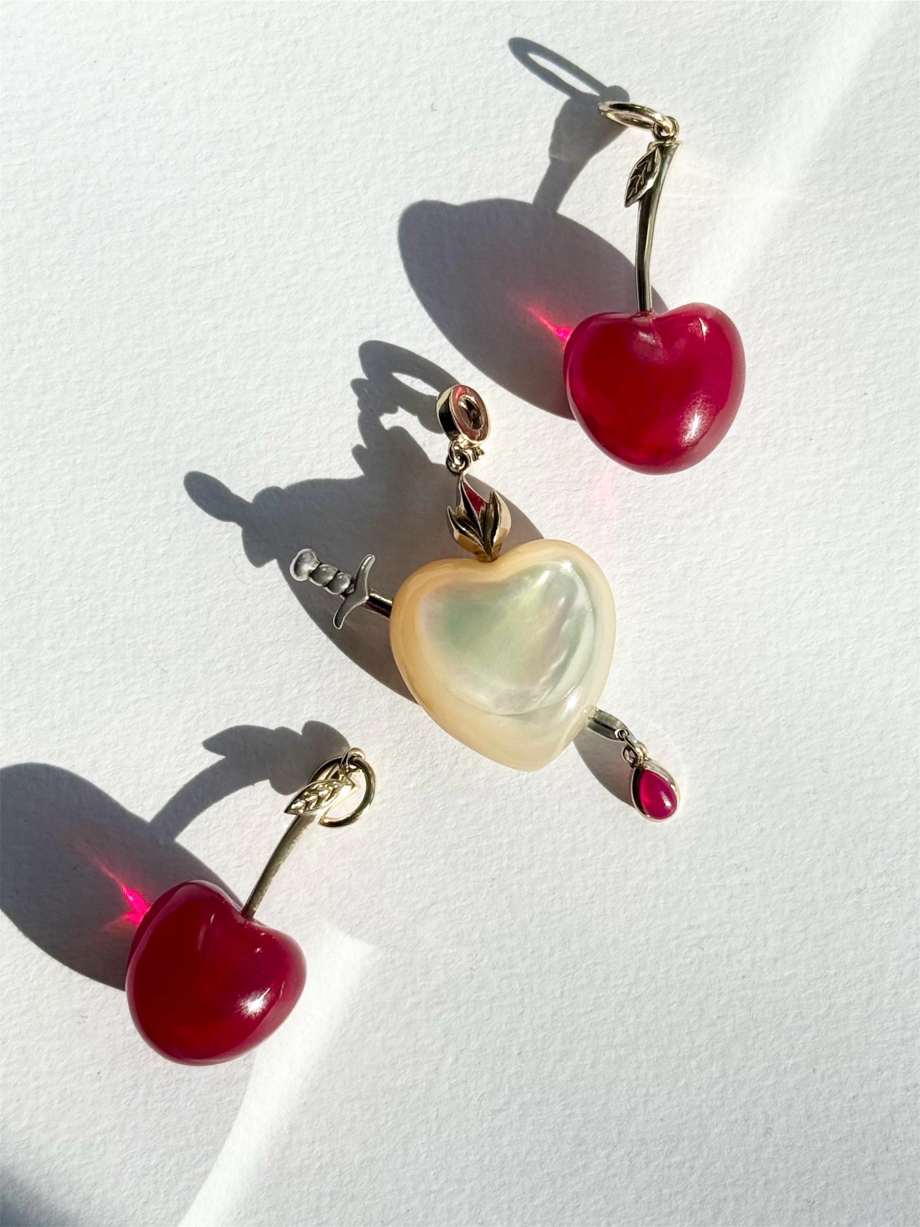Red cherry charms and pearl heart charm on a white background. Designed by Maura Green