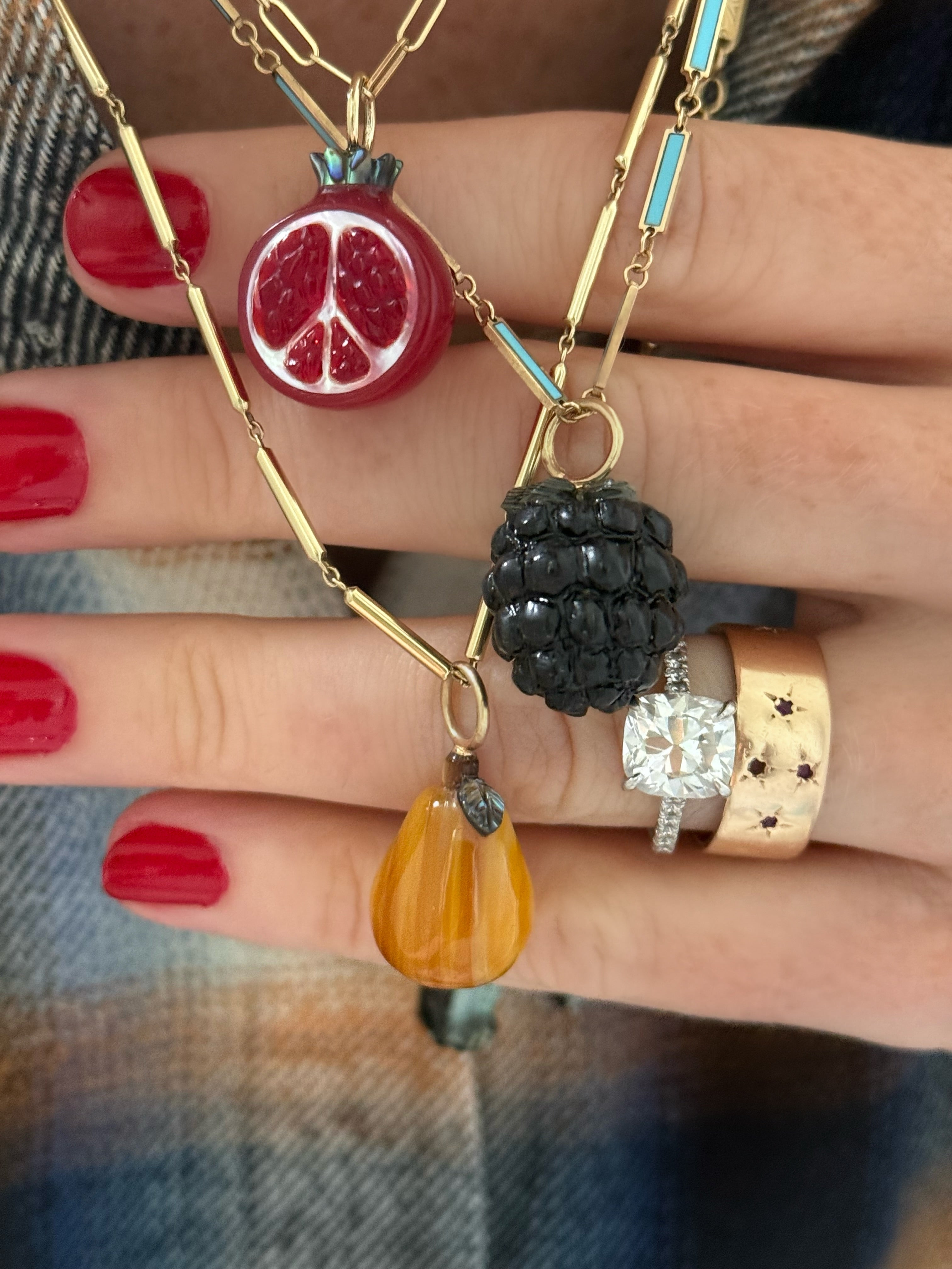 Hand wearing multiple gold necklaces with fruit-themed pendants on a blurred background