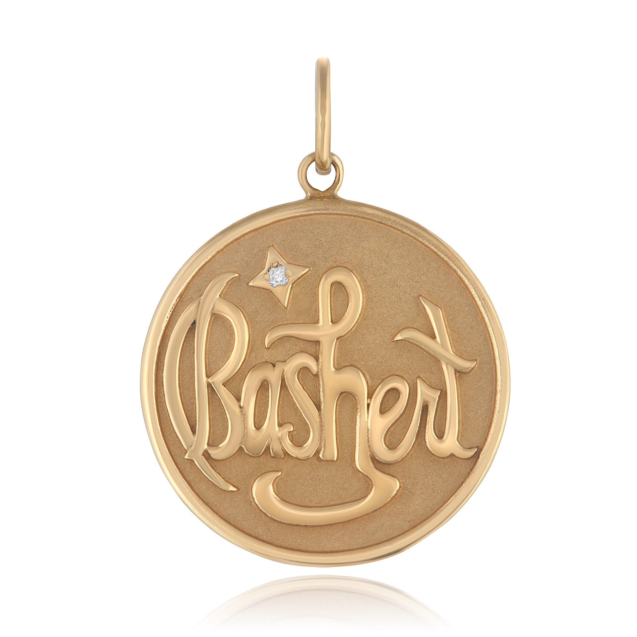 A 14K gold circular medallion with the word 'BASHERT' engraved in a decorative font designed by Maura Green