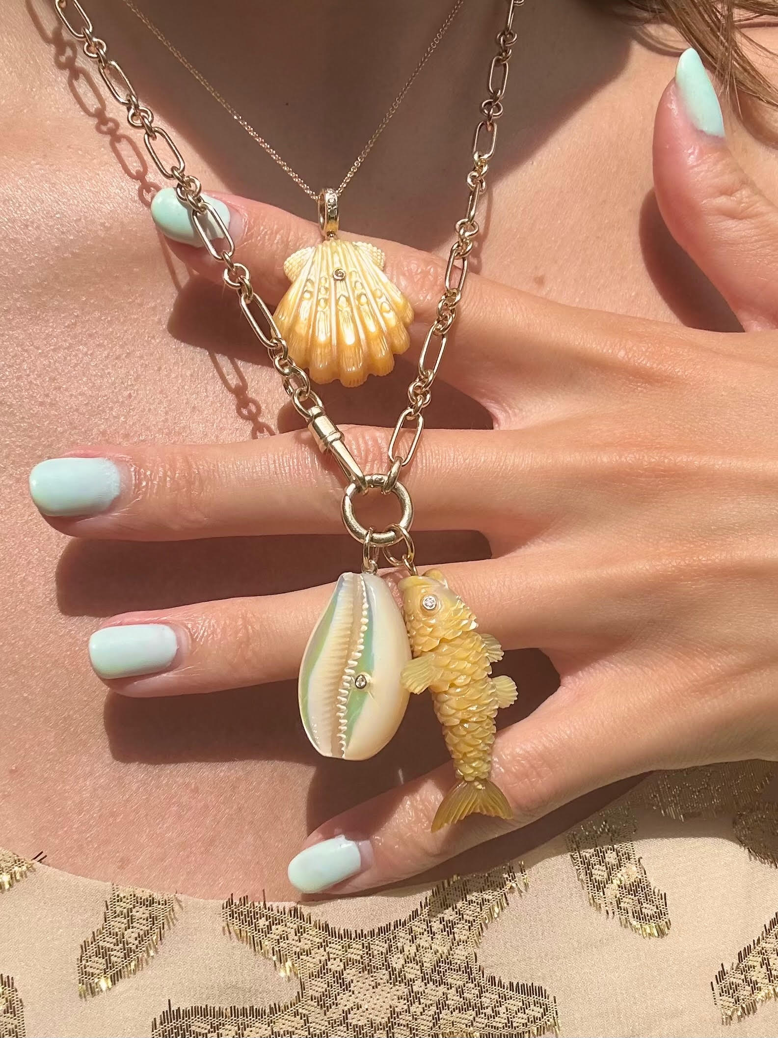 Gold fish-shaped charm with gold chain on model's neck designed by Maura Green
