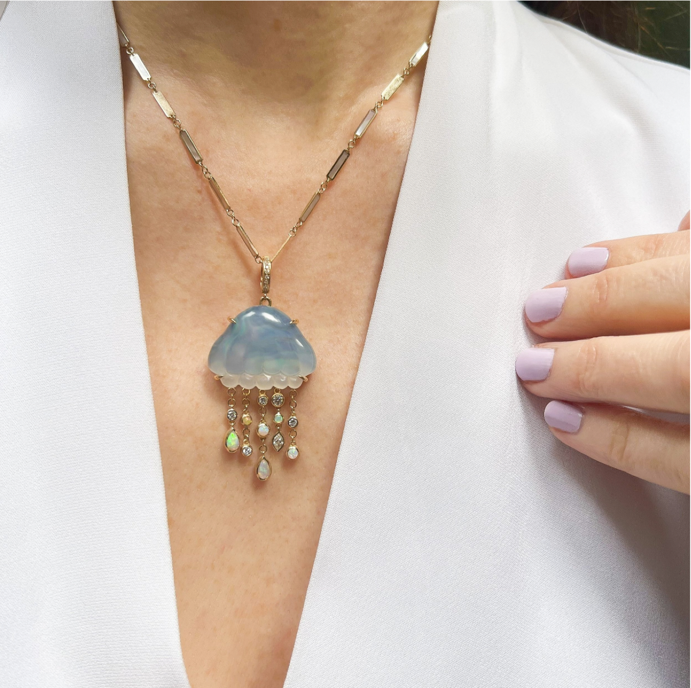 A bio luminescent jellyfish necklace with hand carved chalcedony over abalone, set in 14K yellow gold. It features dangling tentacles with diamonds and opals. On model's neck designed by Maura Green
