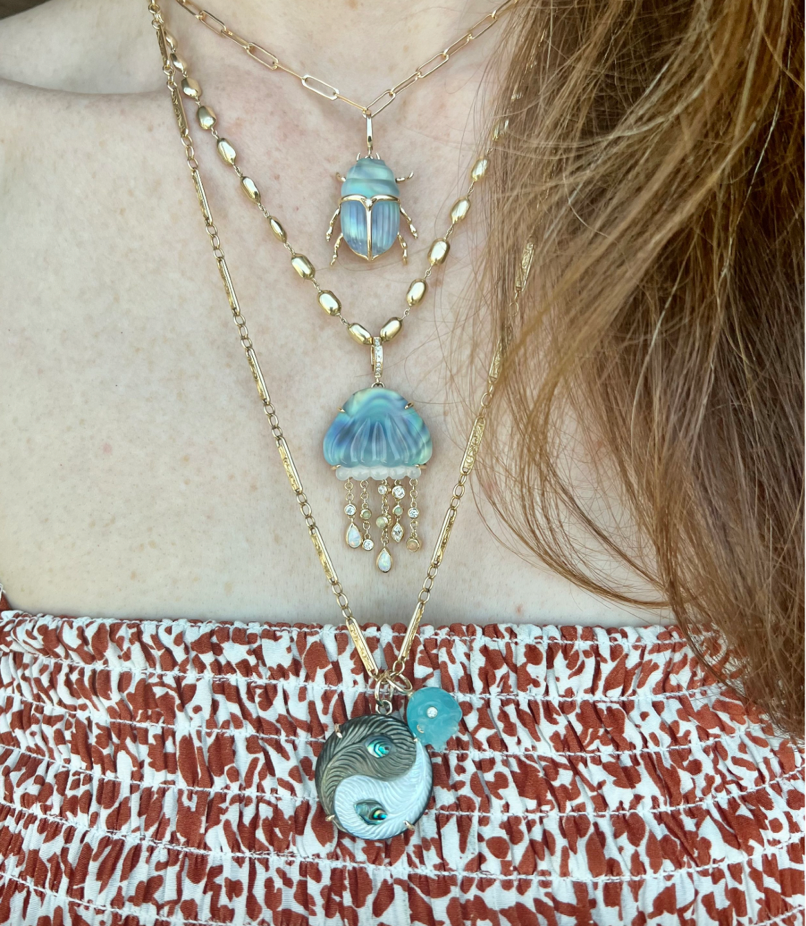 A bio luminescent jellyfish necklace with hand carved chalcedony over abalone, set in 14K yellow gold. It features dangling tentacles with diamonds and opals. On model's neck designed by Maura Green
