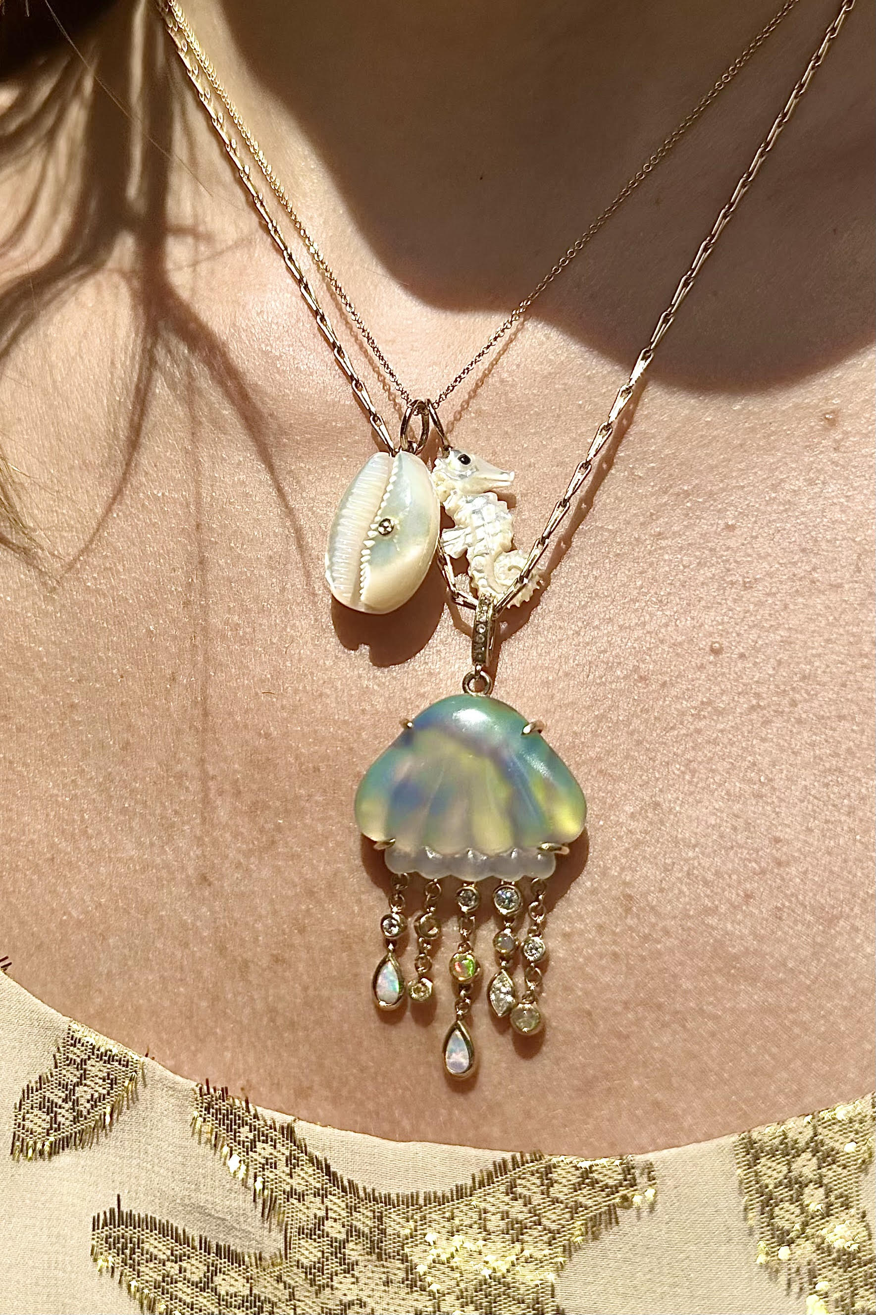 A bio luminescent jellyfish necklace with hand carved chalcedony over abalone, set in 14K yellow gold. It features dangling tentacles with diamonds and opals. On model's neck designed by Maura Green