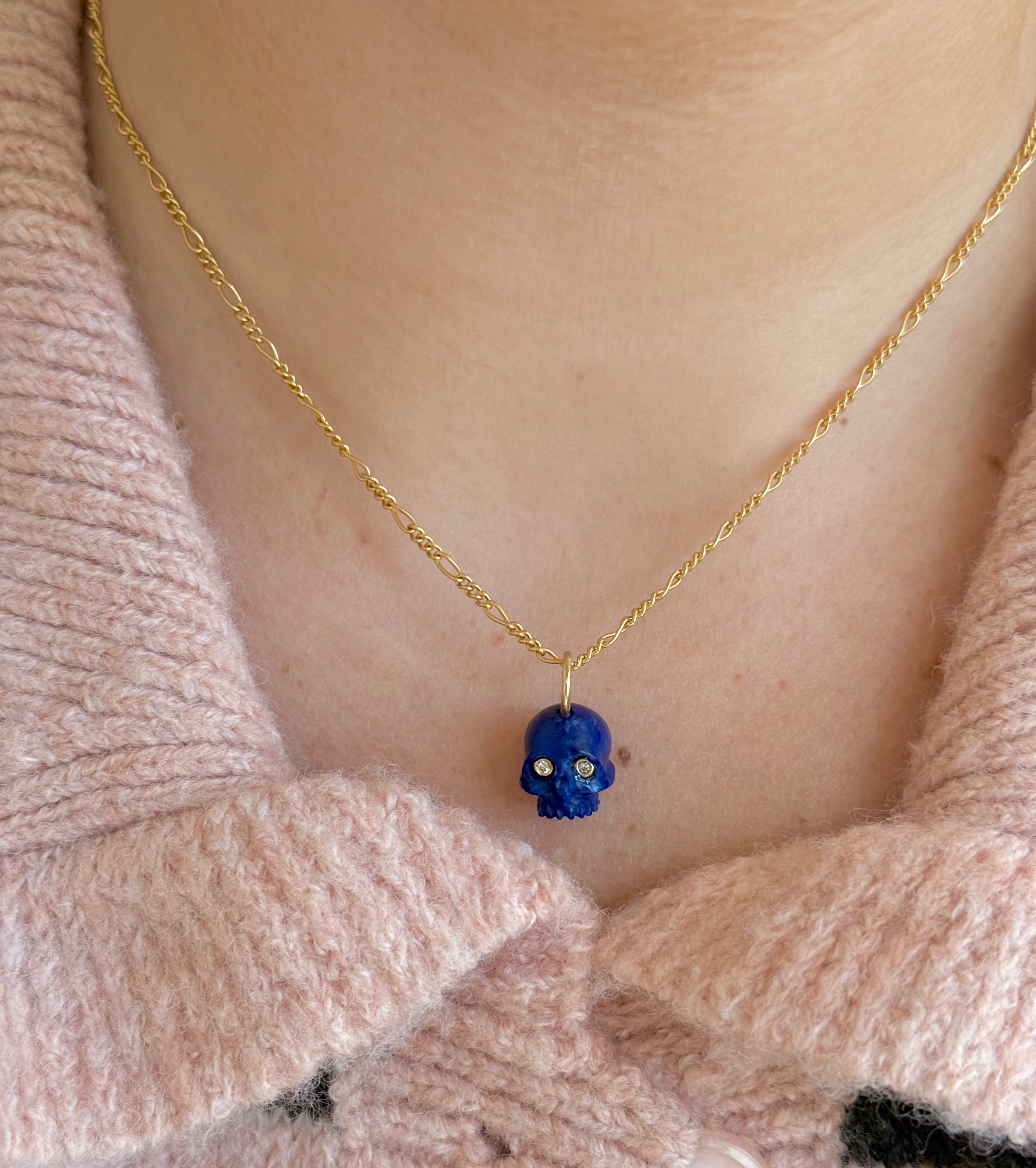 Necklace with a blue lapis skull pendant worn by a person wearing a pink sweater.