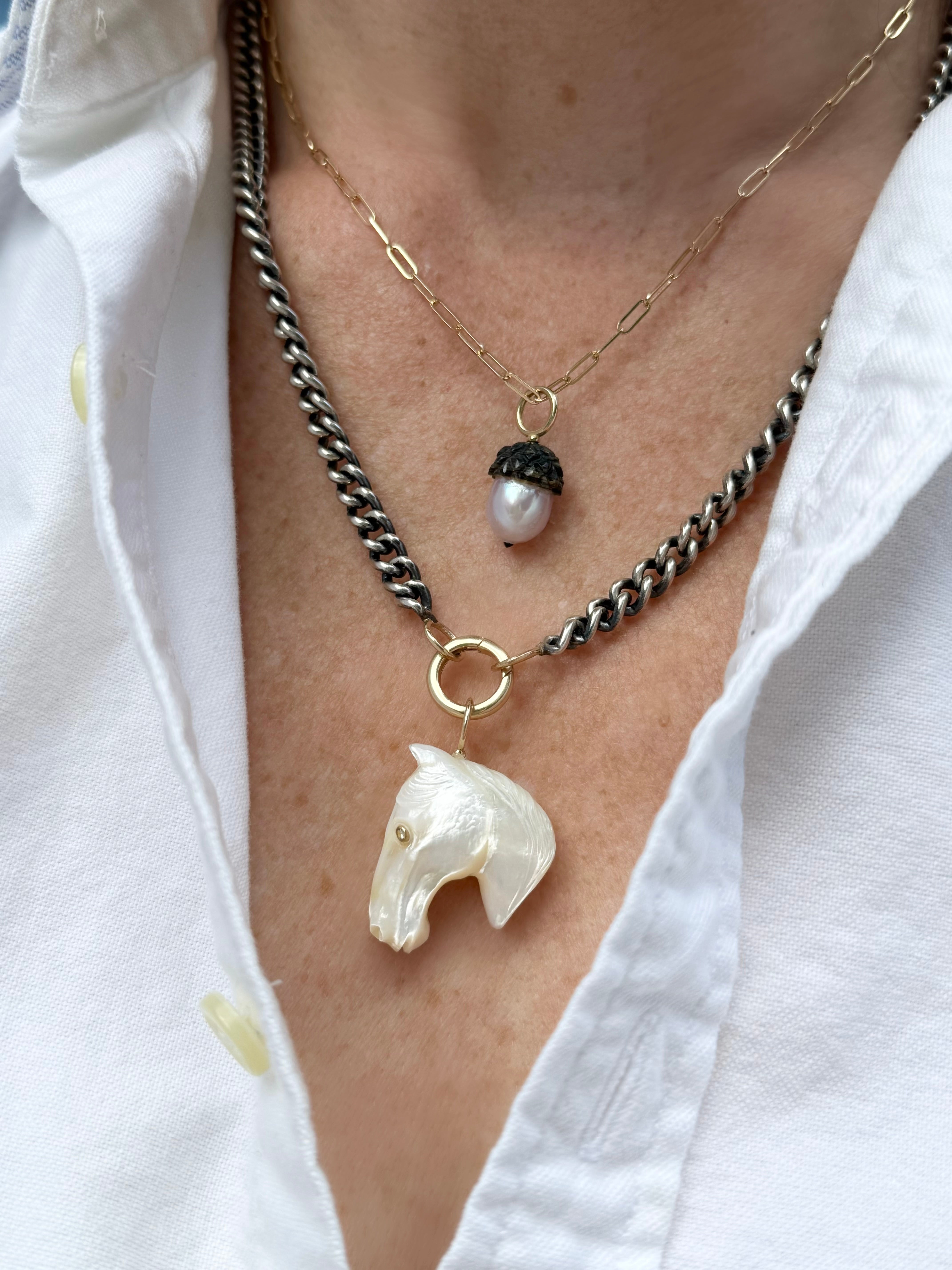 Necklace with horse-shaped pendant and an acorn shaped pearl drop on a white shirt background
