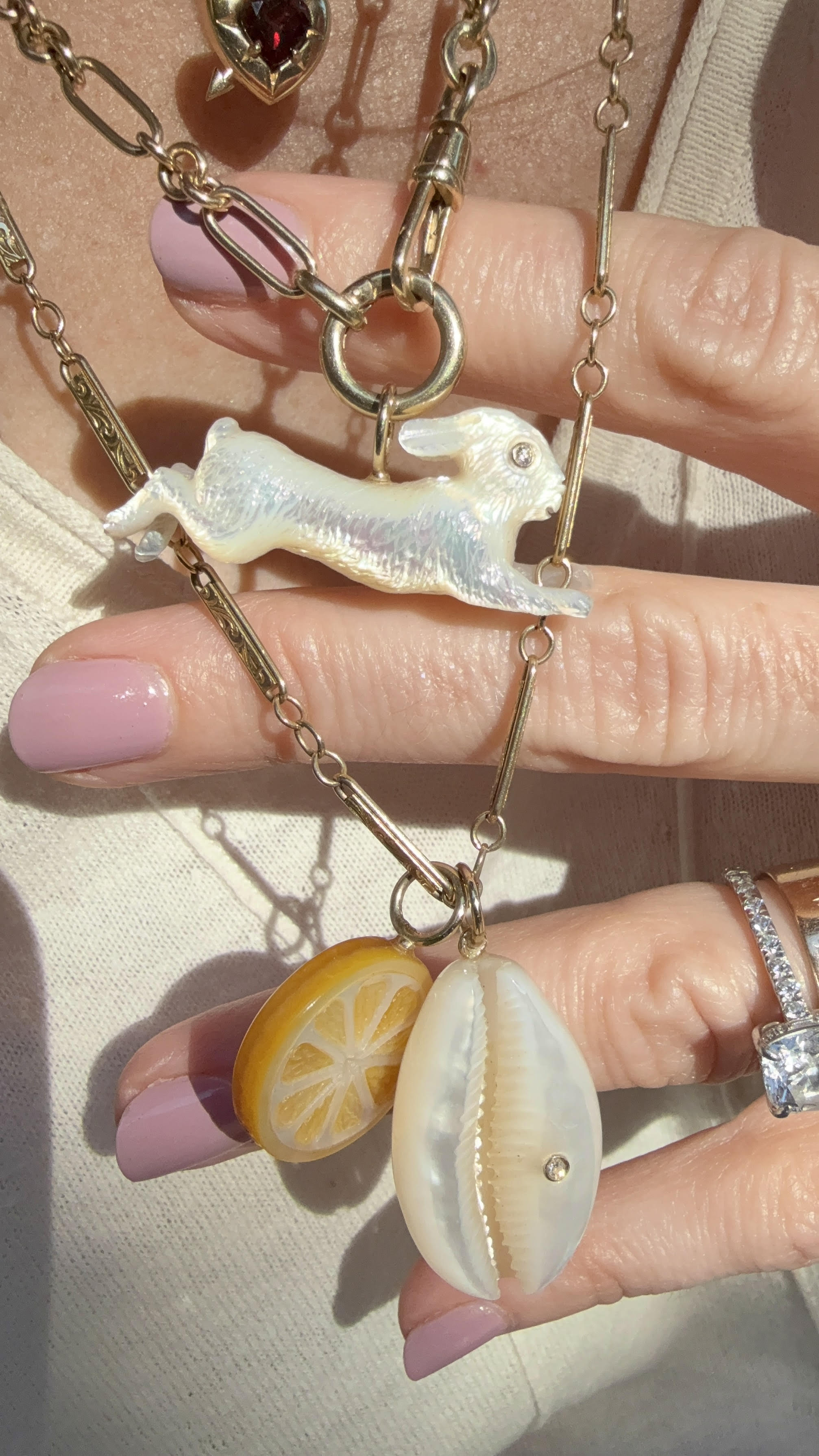 Layered necklaces with charms including white mother of pearl leaping bunny rabbit on a gold chain. Designed by Maura Green