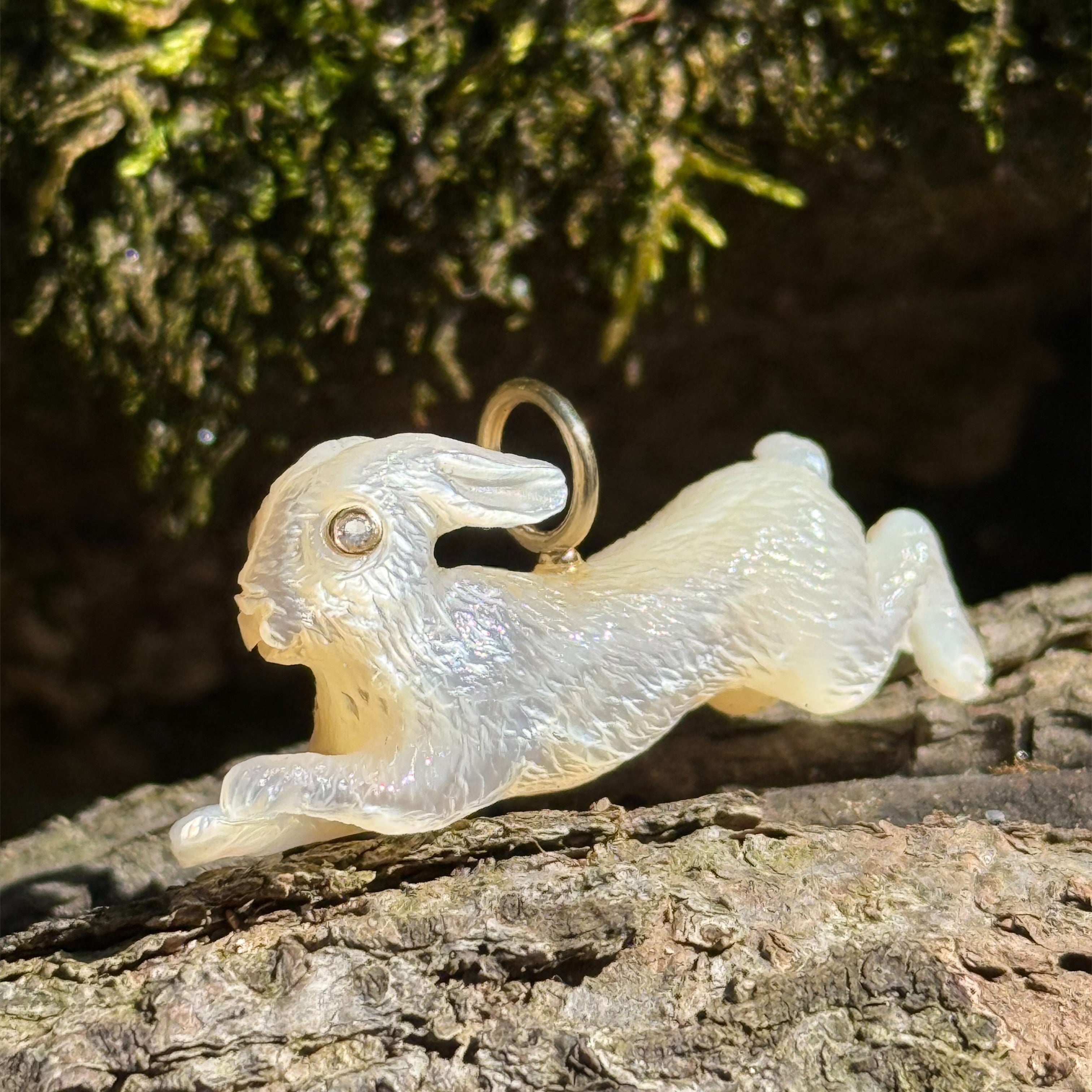 White mother of pearl leaping bunny rabbit charm on a natural background. Designed by Maura Green