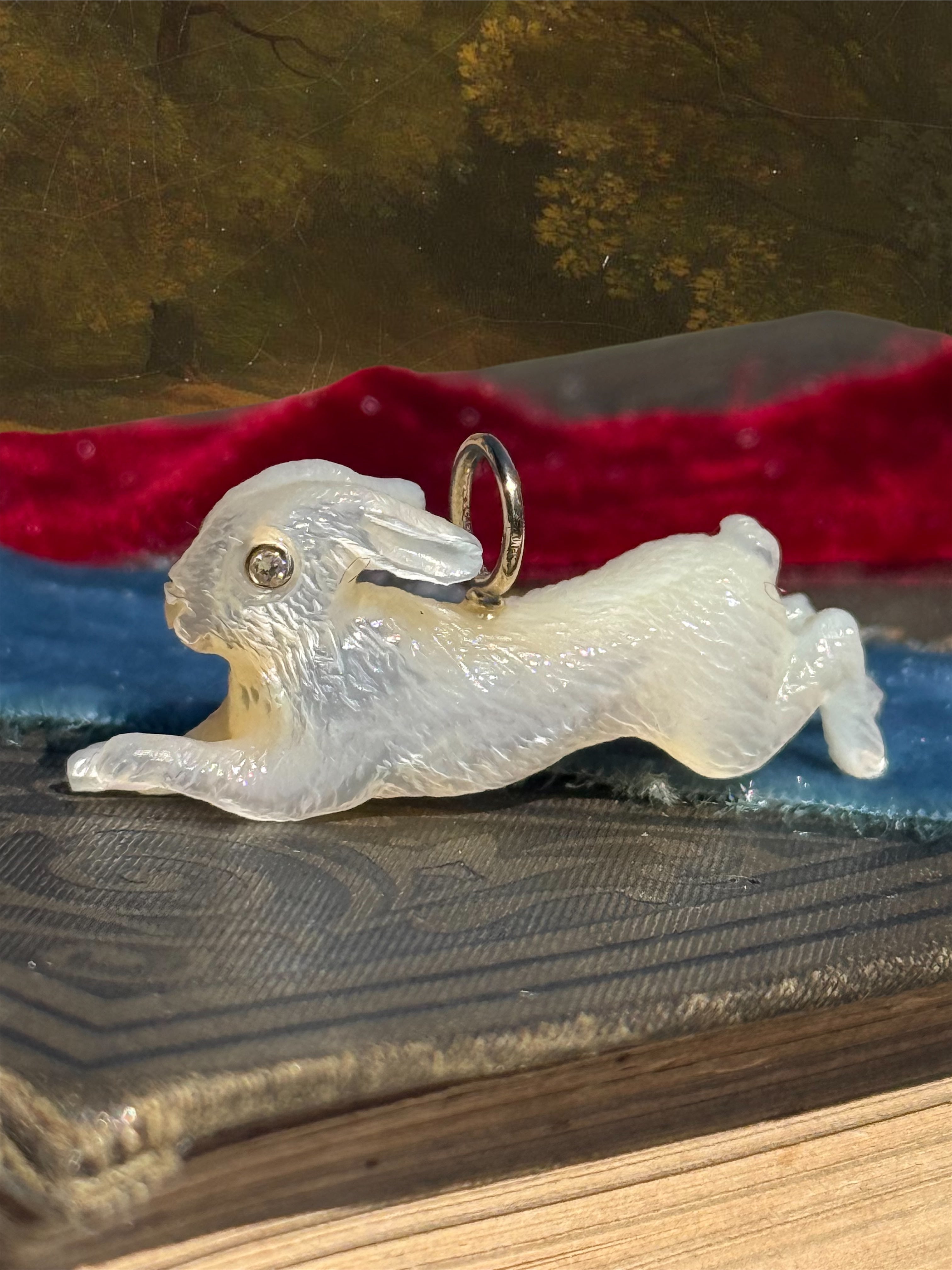 White leaping rabbit charm on a textured surface with a blurred natural background. Designed by Maura Green