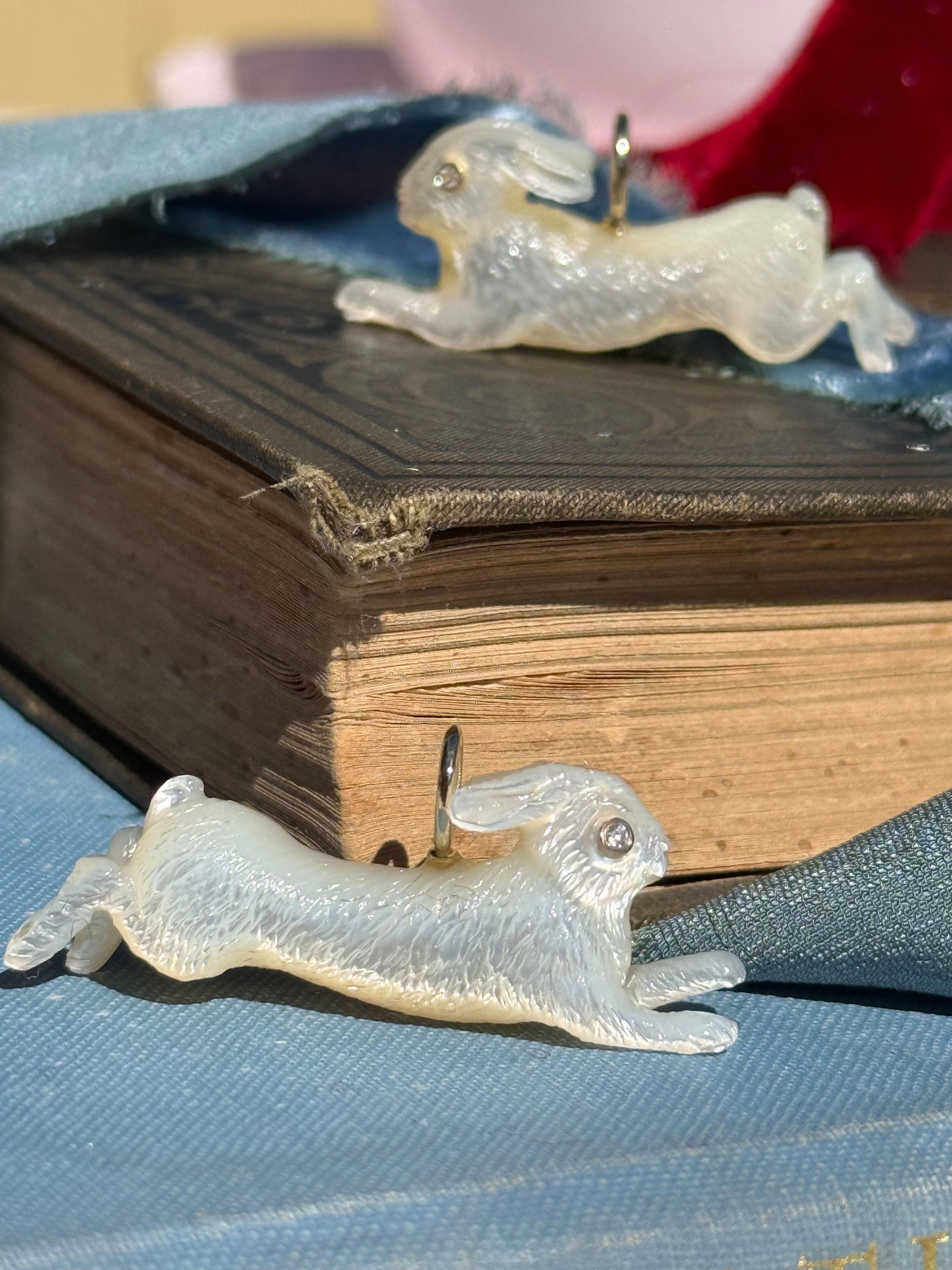 Two white leaping rabbit charms on a blue, textured background. Designed by Maura Green