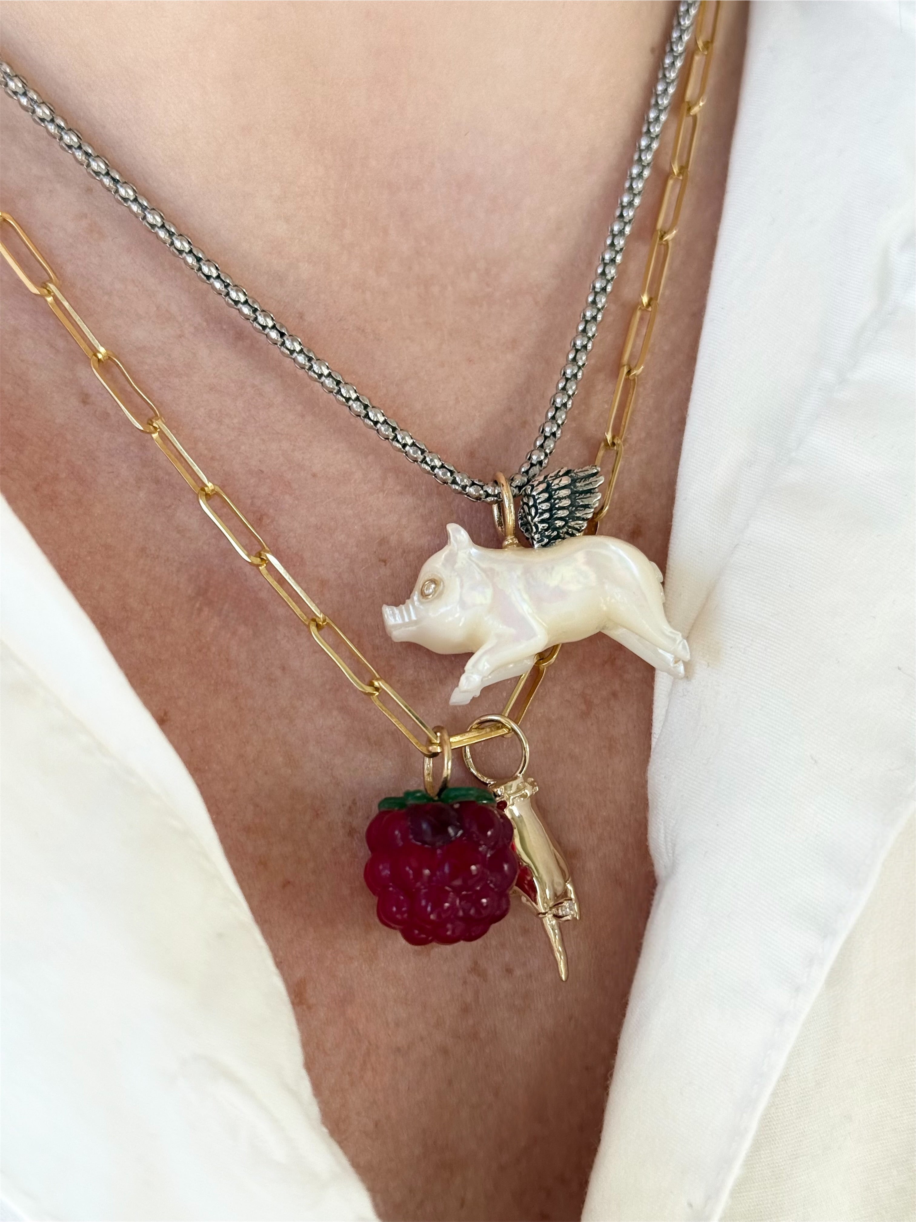 Necklace with a pig charm, red berry charm, and gold chain on a person's neck.