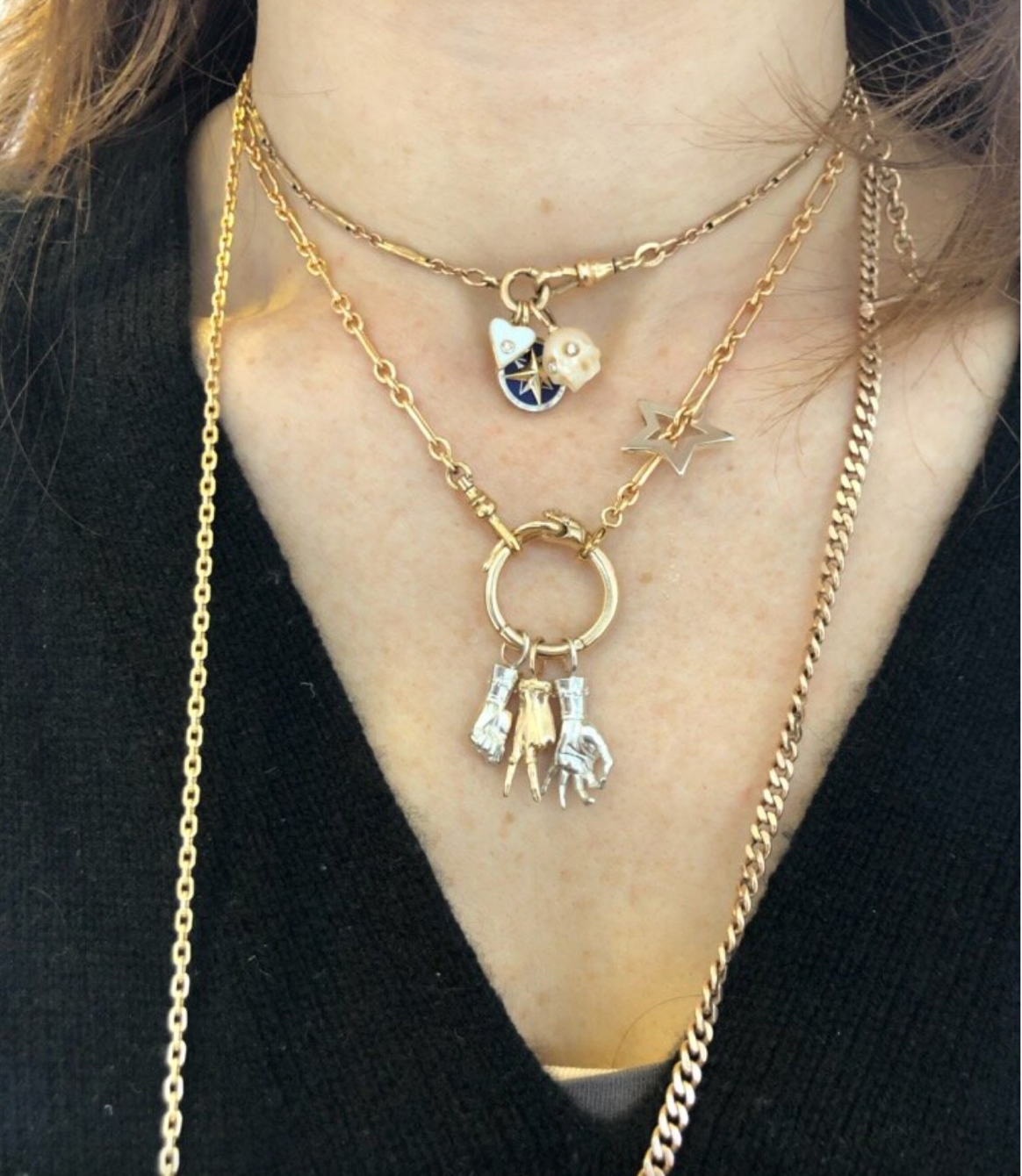 Cropped shot of a person wearing a necklace with a circular charm holder with 3 figural hand charms including a figa, a peace sign, and a mudra.