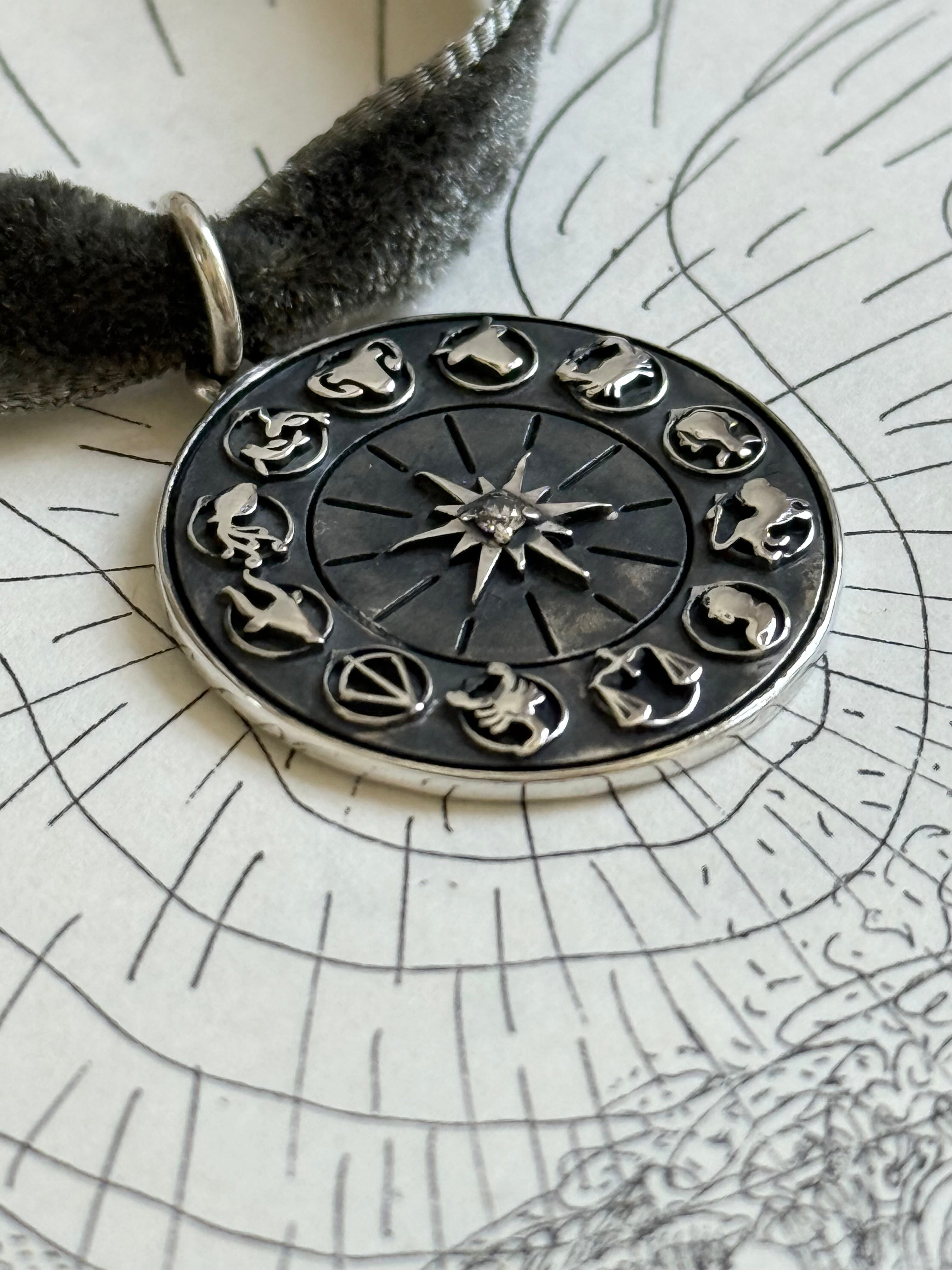 Silver zodiac charm pendant designed by Maura Green Jewelry on a textured surface with star map background