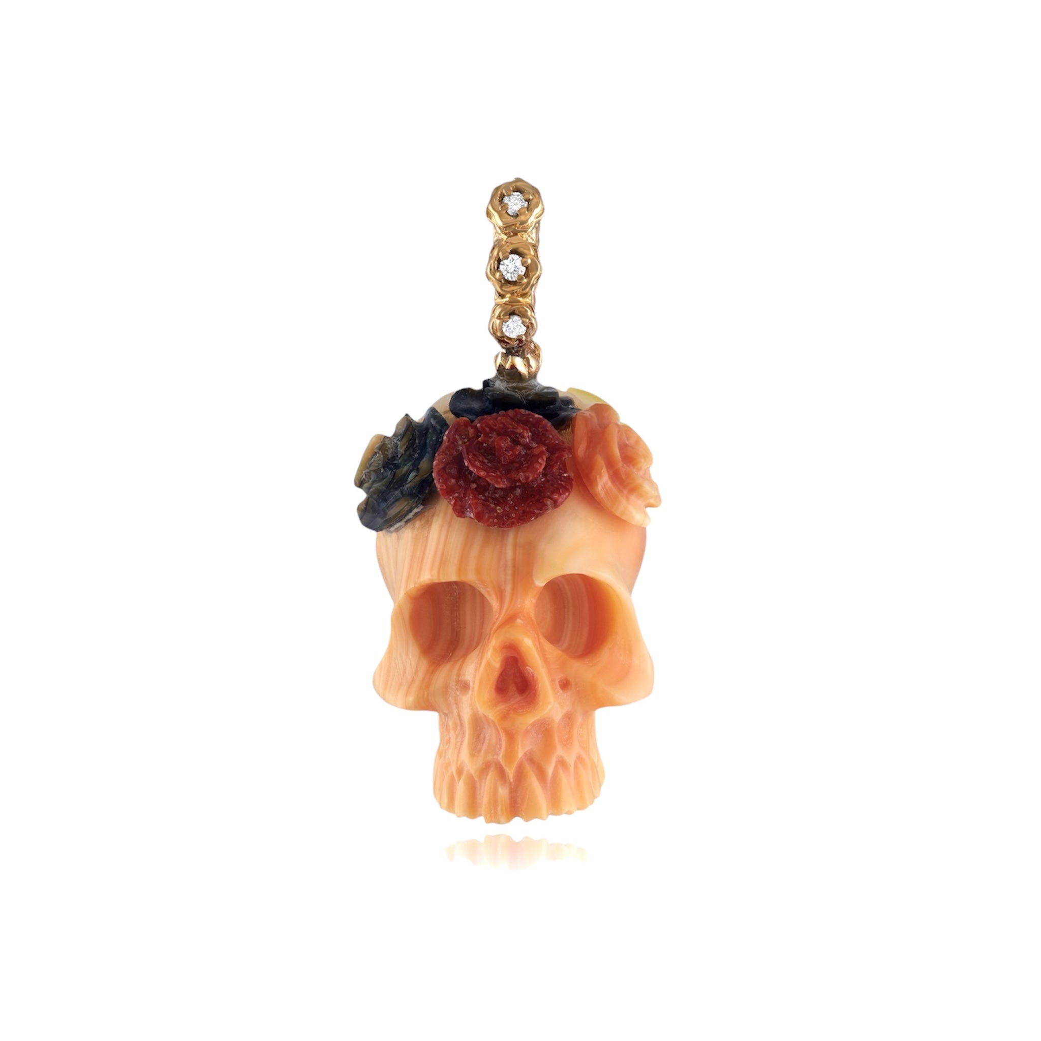 A coral colored carved 3 dimensional skull charm with a crown of semi precious stone and shell flowers and a gold and diamond bail against a white background.