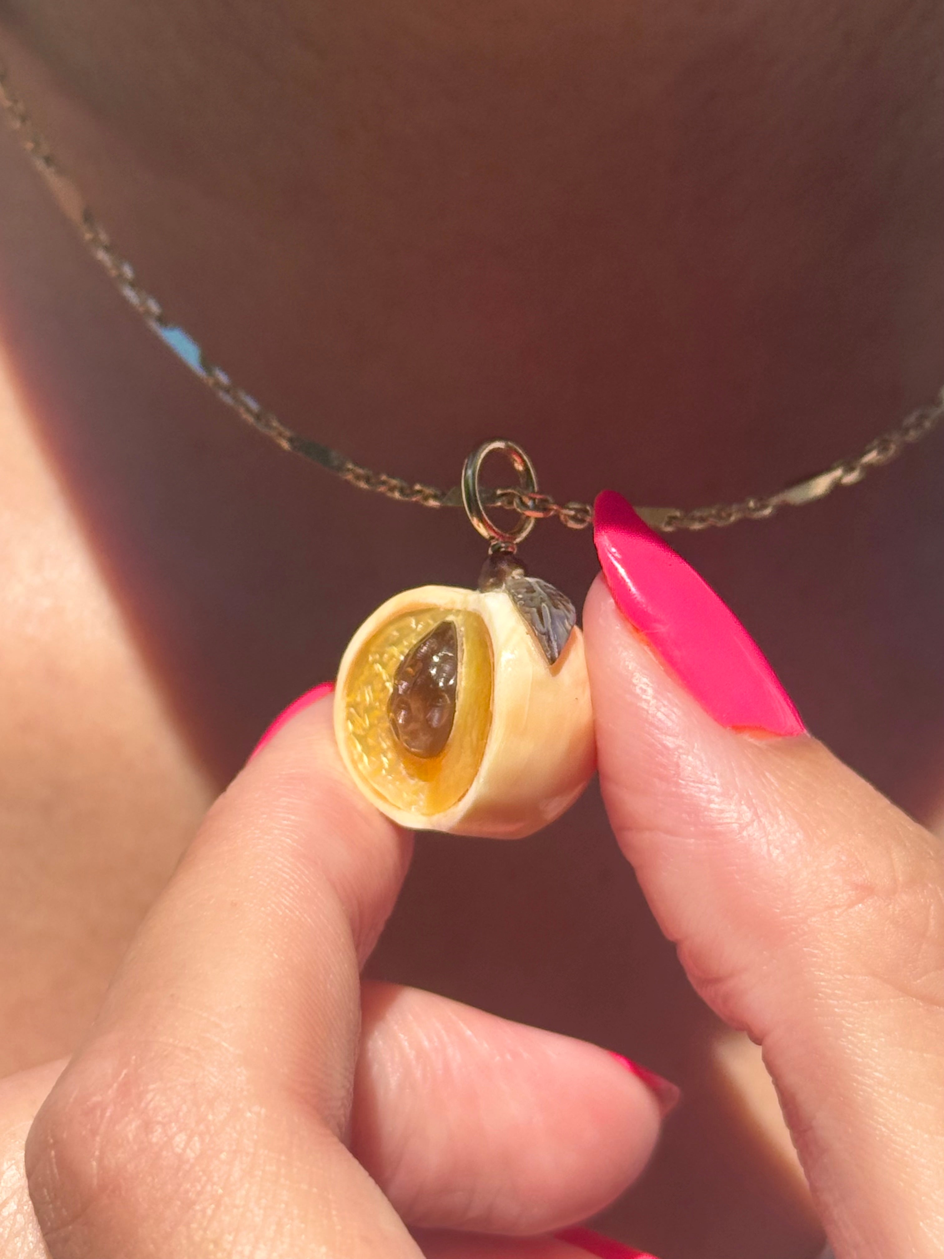 Peach Charm close up on a gold chain worn by model. Designed by Maura Green