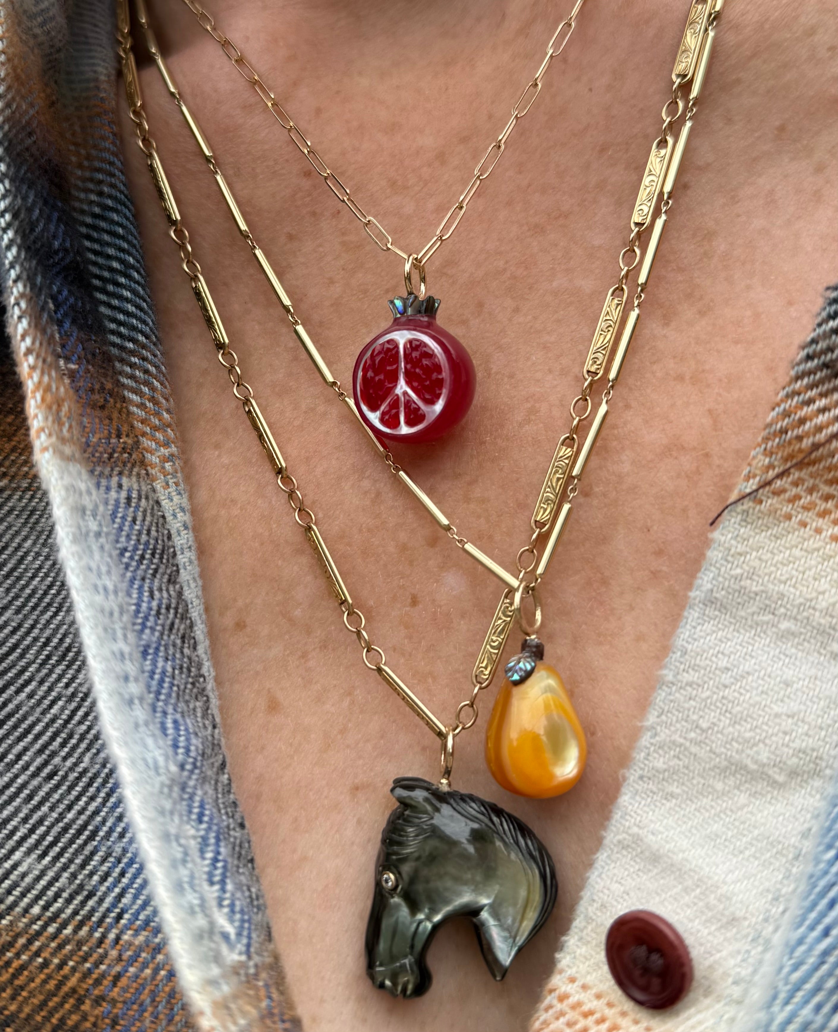 Necklace with a black horse head pendant, a golden pear pendant, and a red pomegranate pendant on a person wearing a plaid shirt.