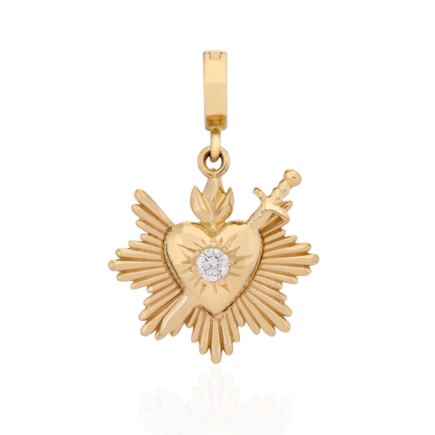 A gold Sacred Heart pendant featuring a heart with radiating rays, a small diamond at the center, and a sword embedded in the side, shown on a white background. Designed by Maura Green Jewelry.