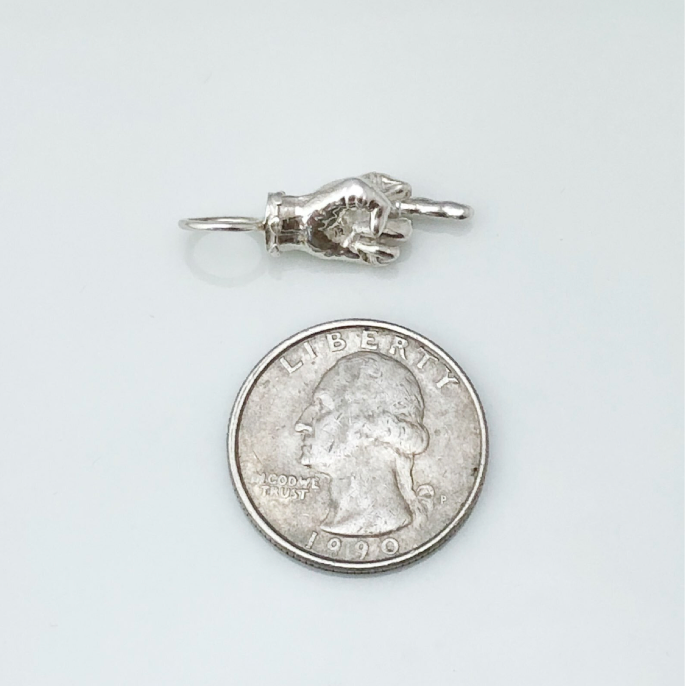 Maura Green Jewelry silver Ladybird charm displayed on a white surface next to a quarter for scale