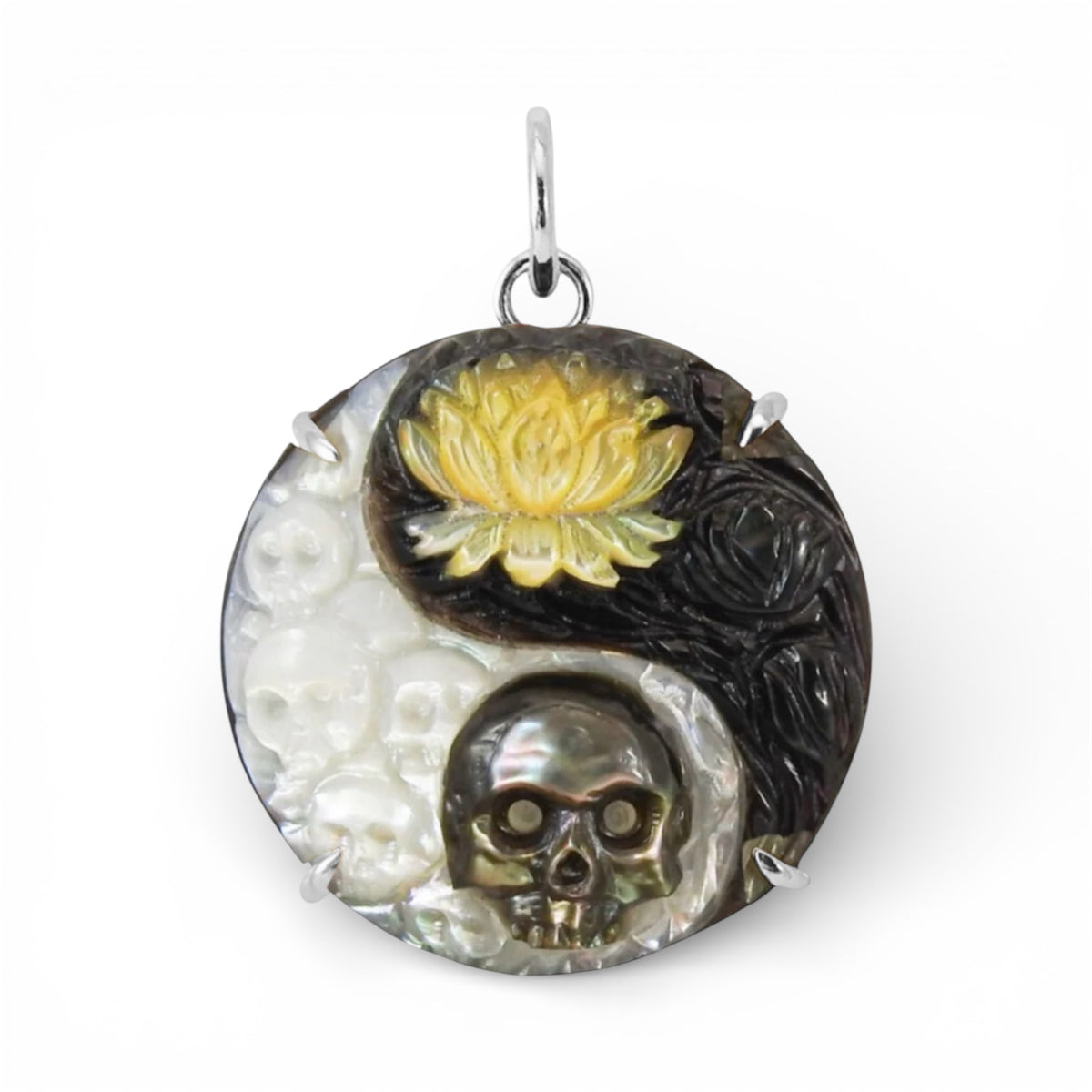 Round hand-carved mother-of-pearl pendant featuring skulls, a golden lotus flower, and dark floral details, finished with a silver bail against a white background.