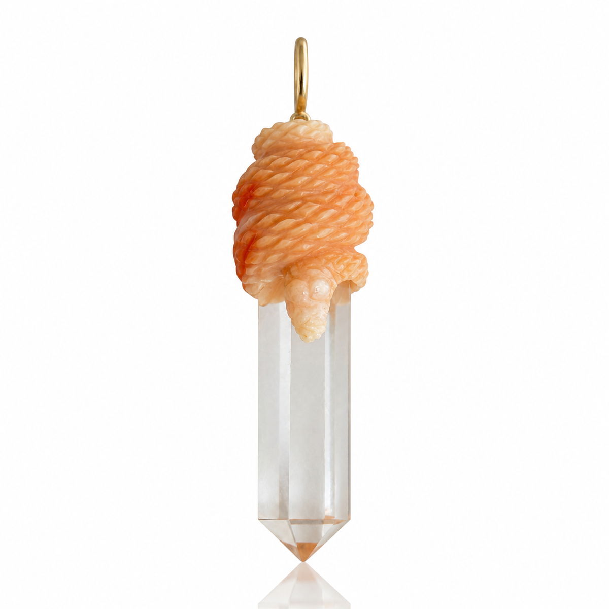 Hand-carved apricot conch shell wrapped around a clear chalcedony crystal point with a 14K yellow gold bail.  Background is a white reflective surface.