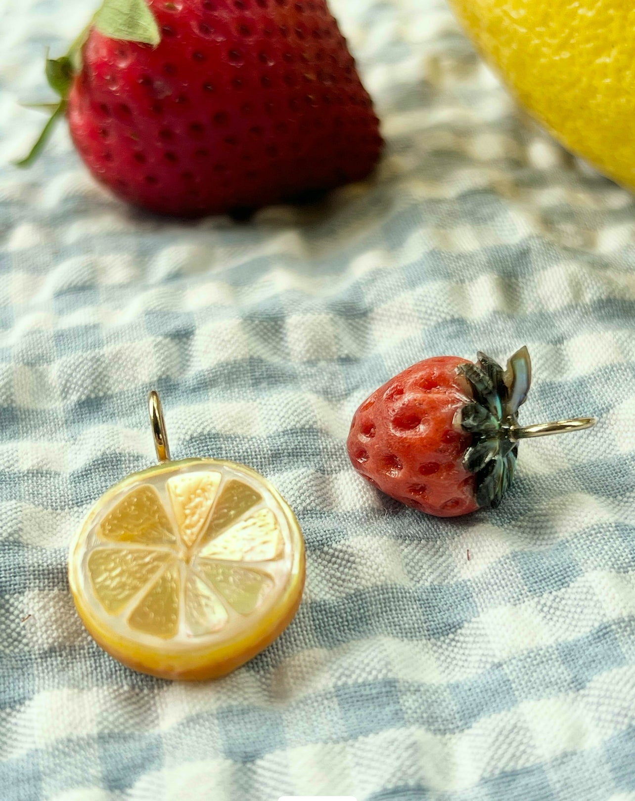 Lemon slice charm on a checkered fabric background with strawberries and a lemon.