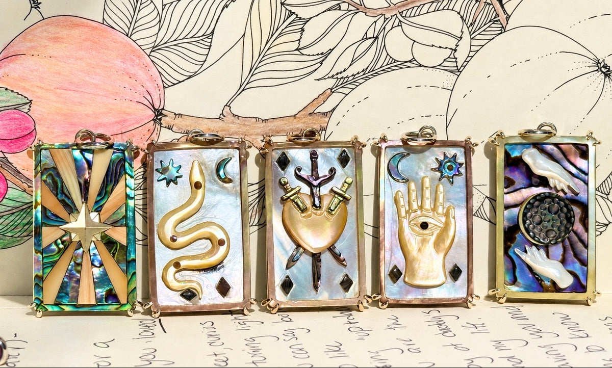 5 hand carved mother of pearl and abalone shell rectangular tarot cards are laid out along a paper illustrated background.