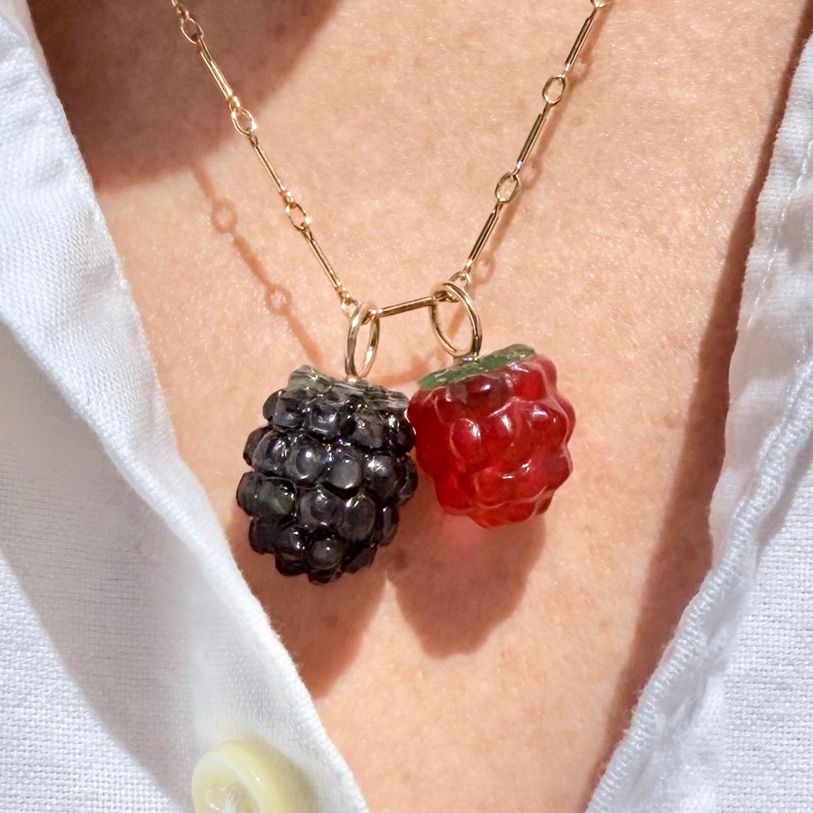 Necklace with blackberry and raspberry pendants on a person wearing a white shirt.