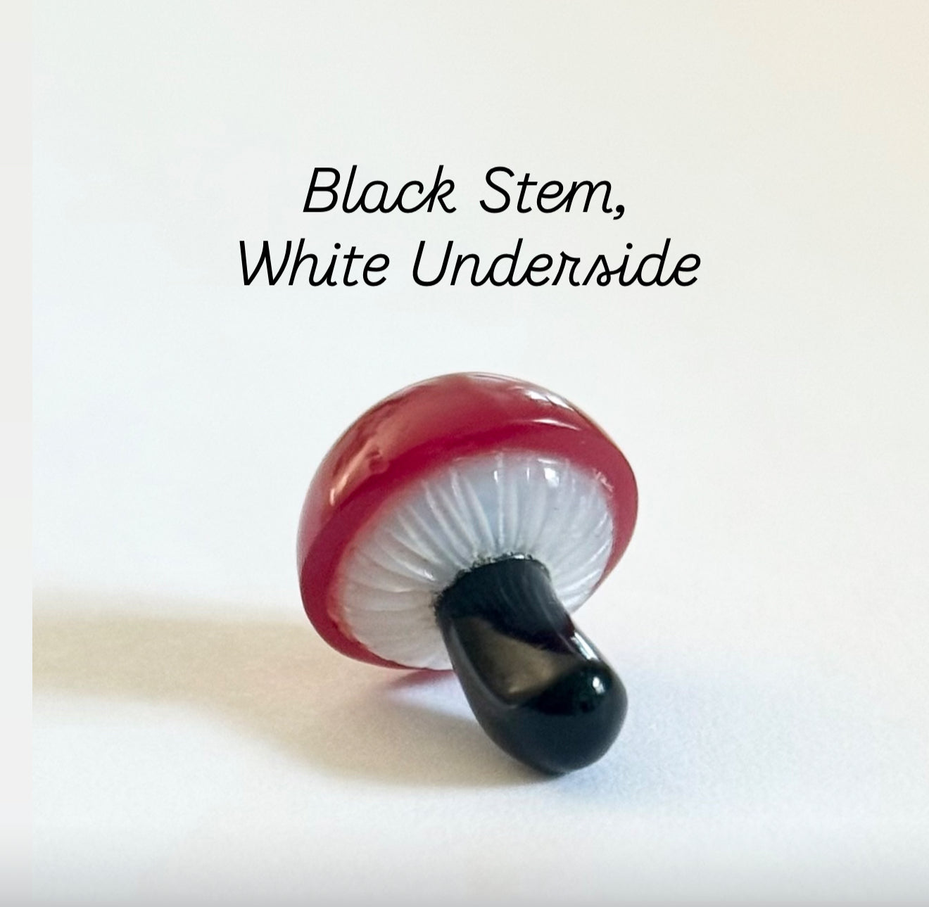 Mushroom charm with black stem and white underside on a white background designed by Maura Green