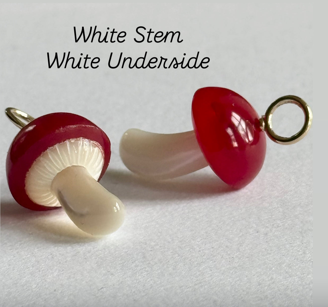 Two mushroom charms with red top and white stem and underside. Designed by Maura Green