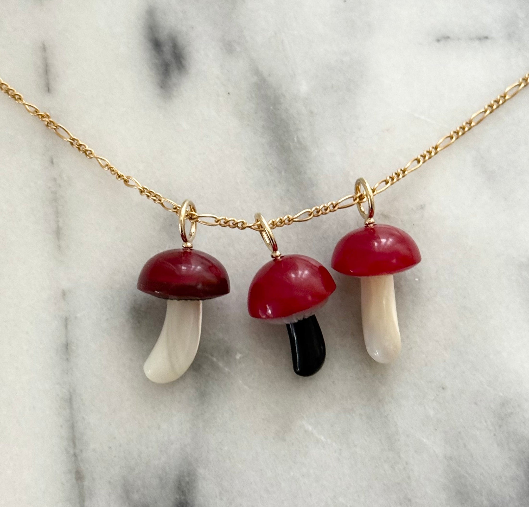 Three mushroom-shaped charm on a gold chain against a marble background