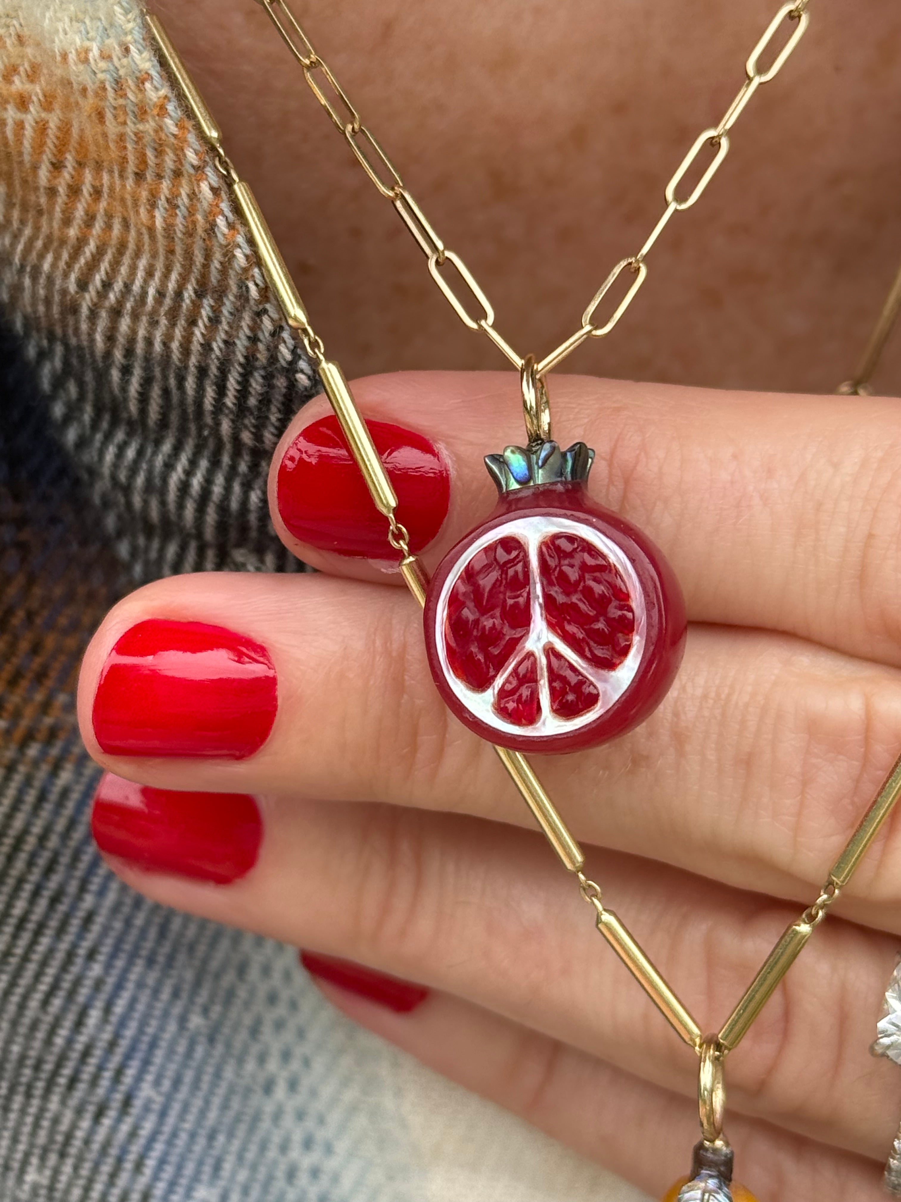 Close-up of a hand wearing a gold chain necklace with a red pomegranate pendant.