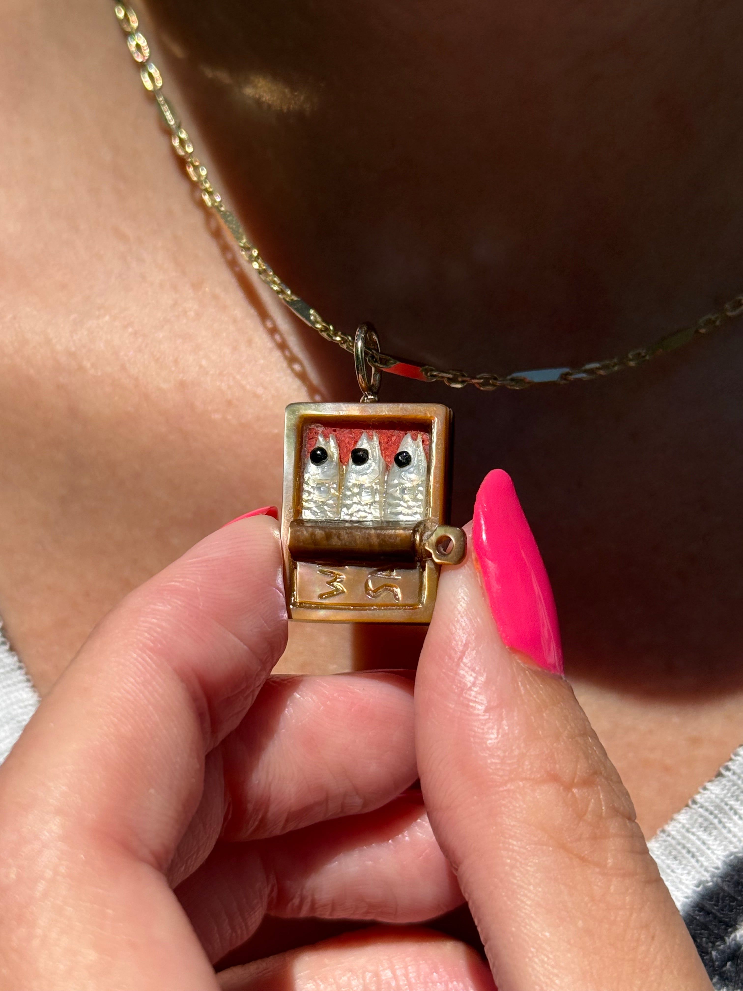 Brown tin with three white sardines on a gold chain worn by model. Designed by maura green