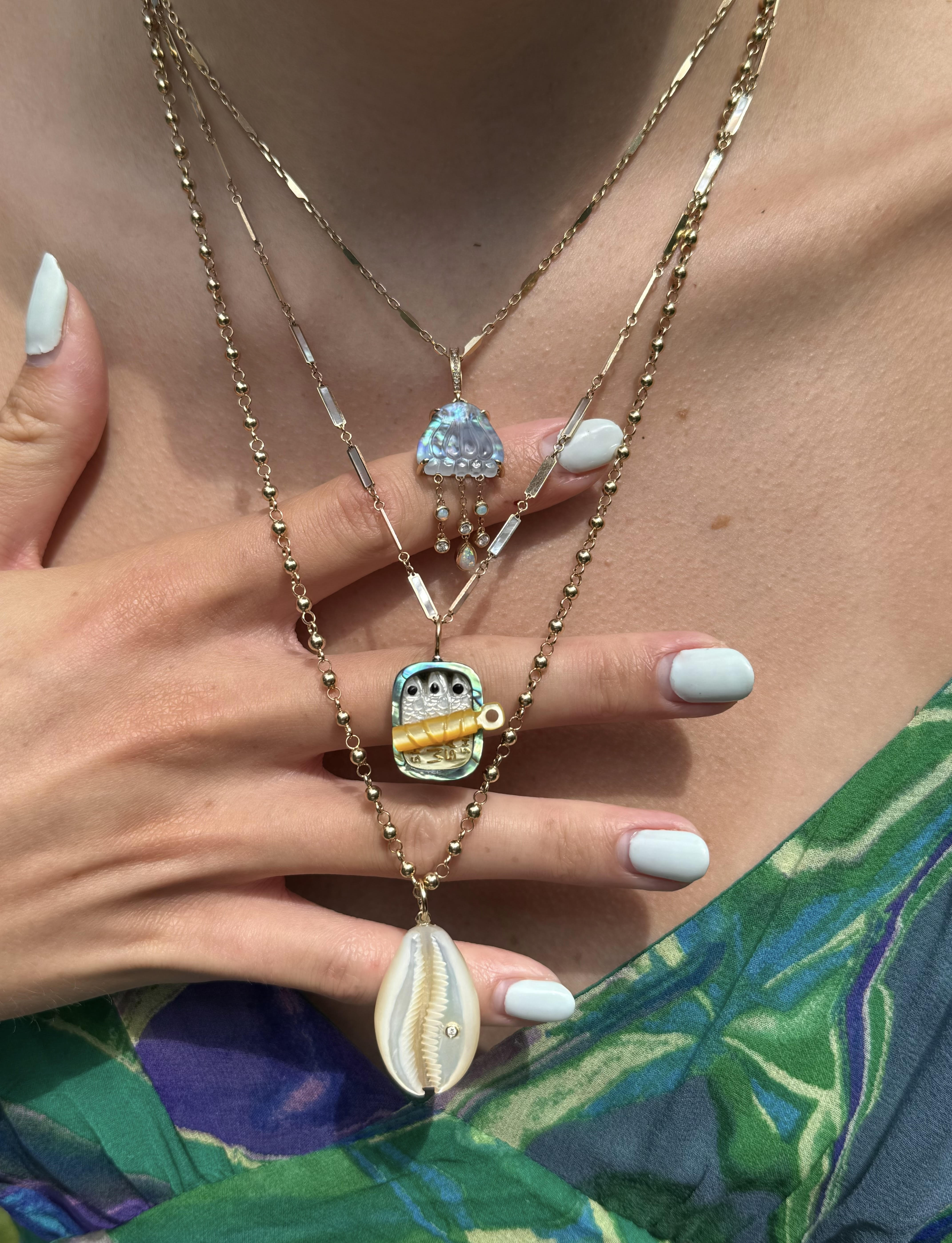 Close-up of a model wearing three necklaces with charms designed by Maura Green. Featuring the sardines tin charm